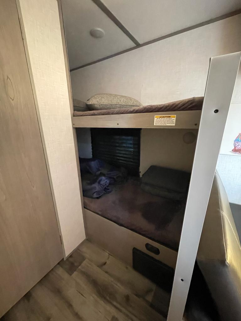 RV rental interior featuring cozy bunk beds. Lower bunk has window, upper has caution label. Ideal for camper travel.. Dutchmen Coleman Lantern LT 2022