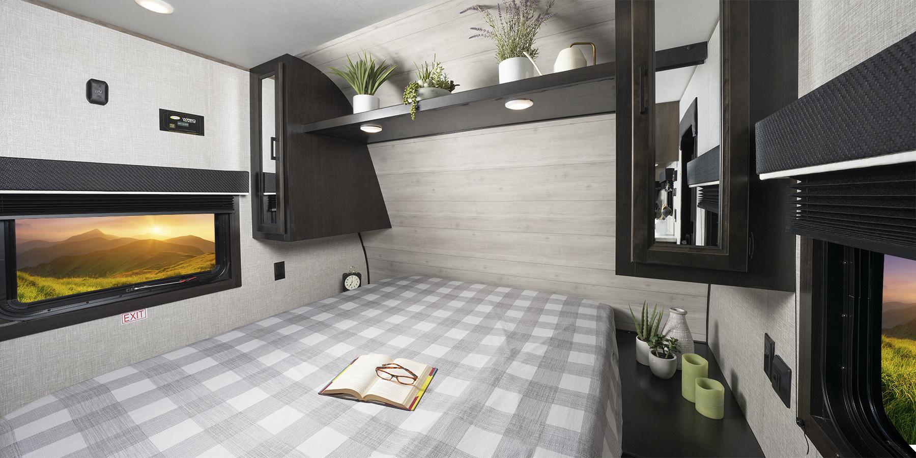 Cozy RV rental bedroom with plaid bed, mountain sunset view, and decorative shelf. Perfect for travel!. Jayco Jay Flight 2023