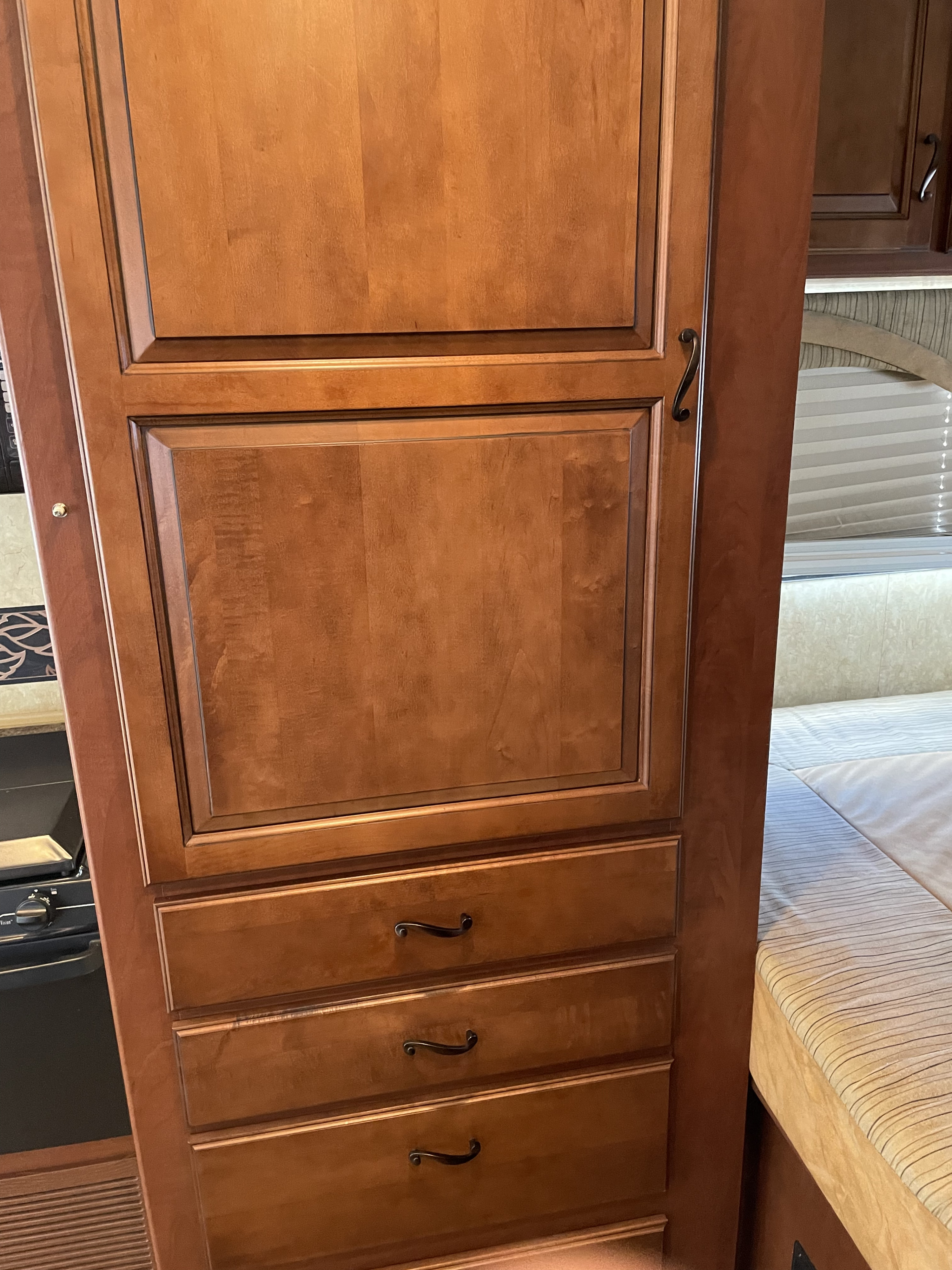RV rental interior: A tall wooden wardrobe with multiple drawers stands beside a bed, near a kitchen area.. Jayco Greyhawk 2011