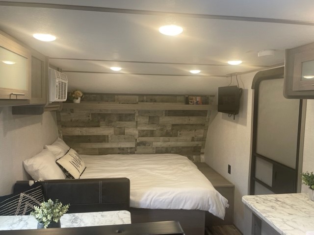 Cozy RV rental bedroom featuring a large bed, decorative wood accent wall, AC unit, and wall-mounted TV.. Dutchmen Coleman Lantern LT 2023