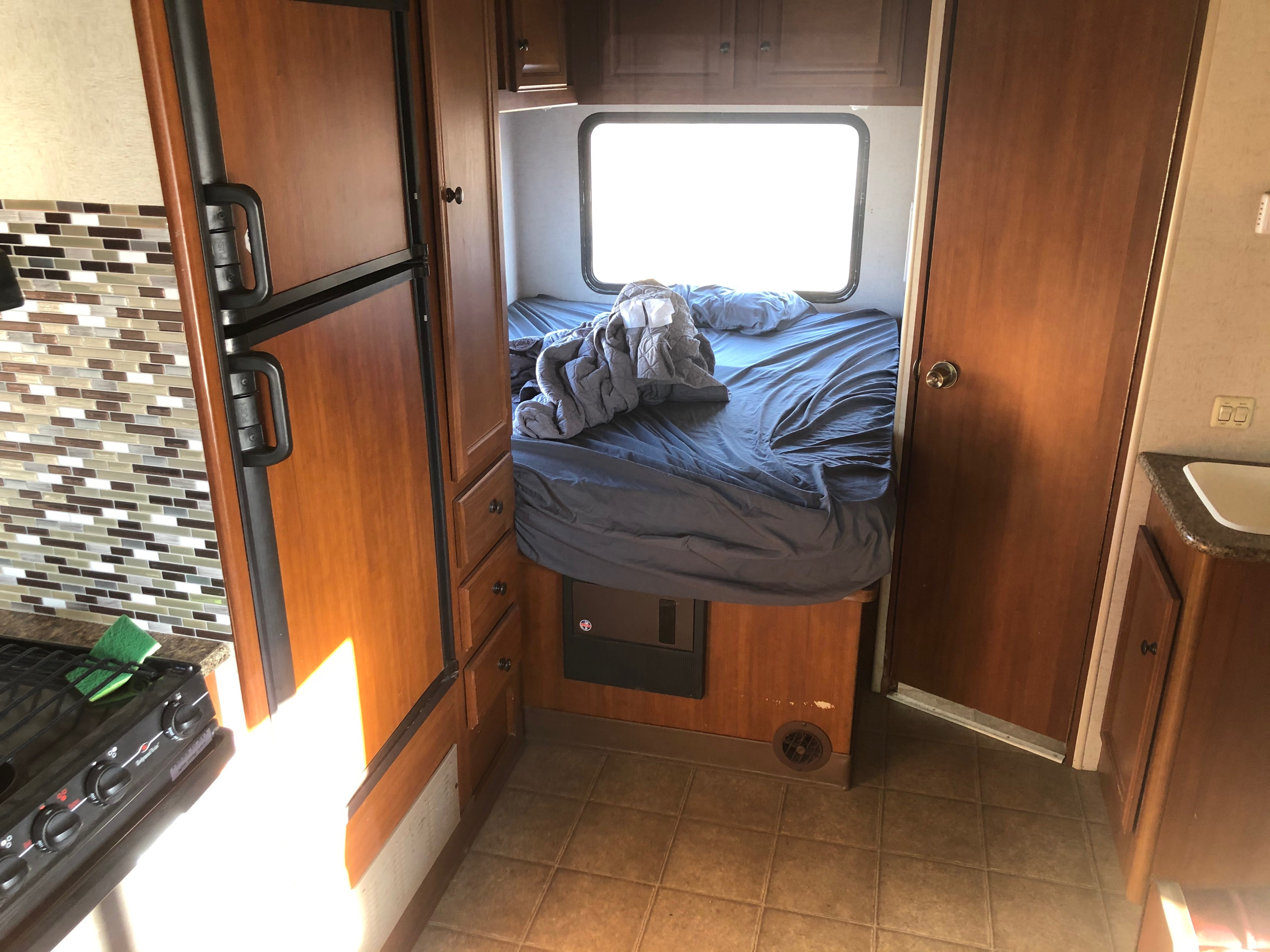 RV rental interior: A compact space showcasing a kitchen (stove, fridge) and a cozy bedroom with a bed.. Fleetwood Tioga Ranger 2014