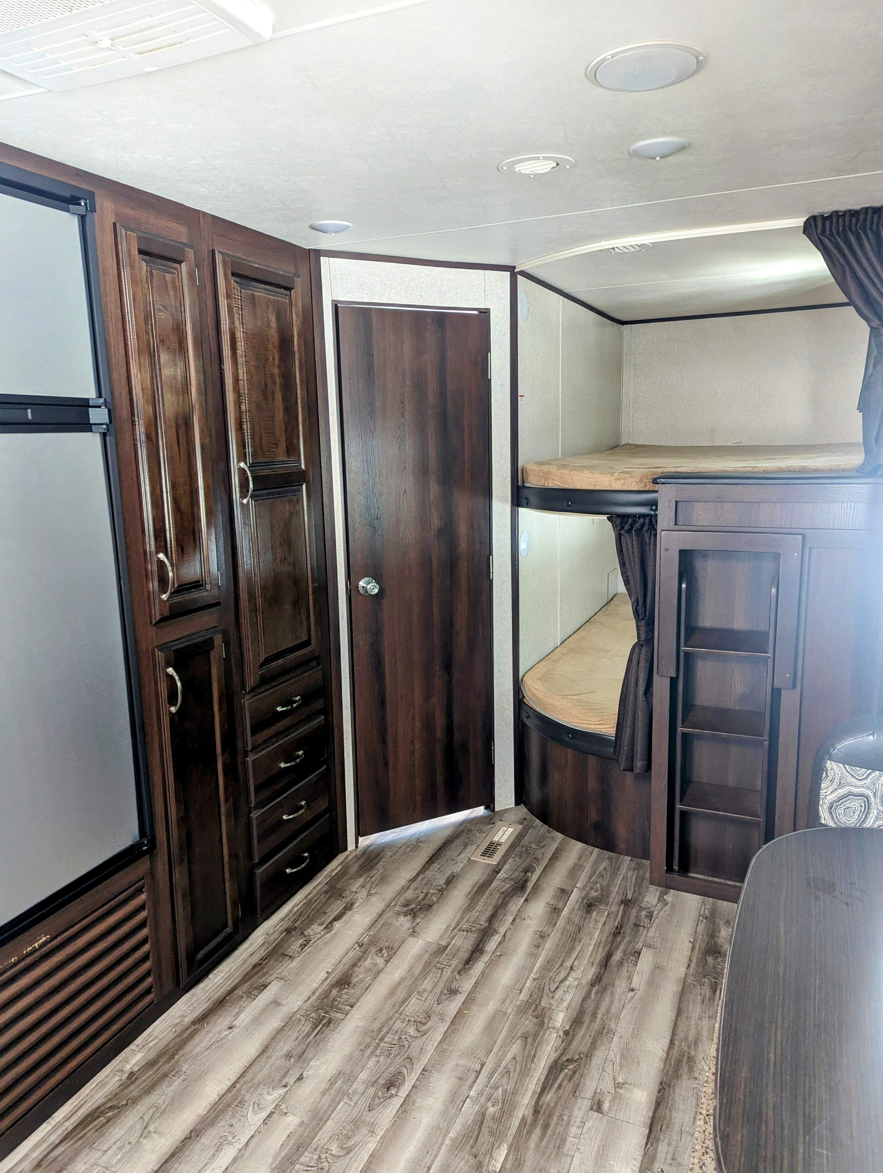 RV rental interior with dark wood cabinetry, refrigerator, a door, two bunk beds, and light wood-look flooring.. Jayco Jay Flight 2018