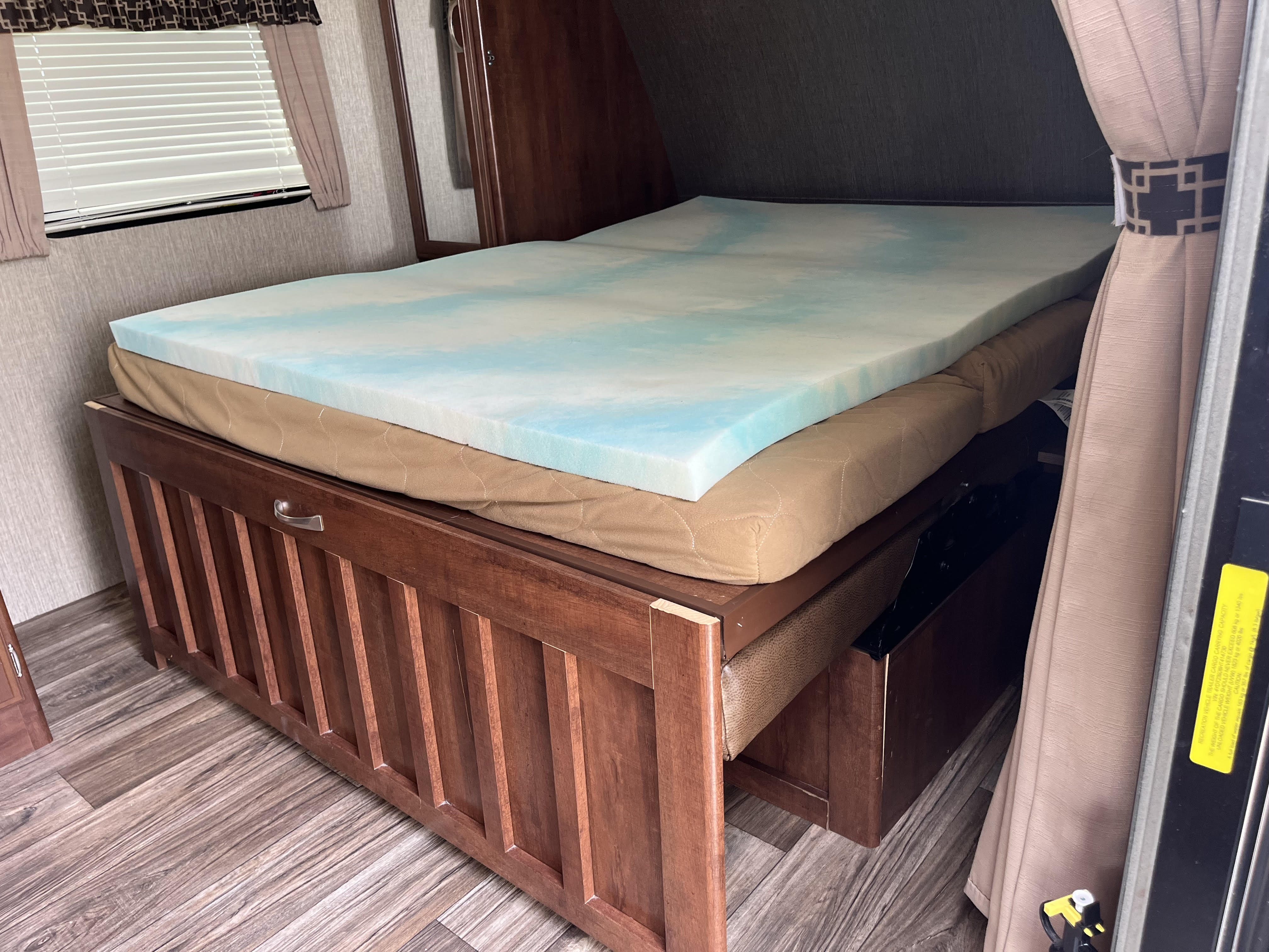 RV rental bedroom: a cozy bed with a blue memory foam topper, rich wood interior, and functional under-bed storage.. Keystone RV Passport 239 ML 2017