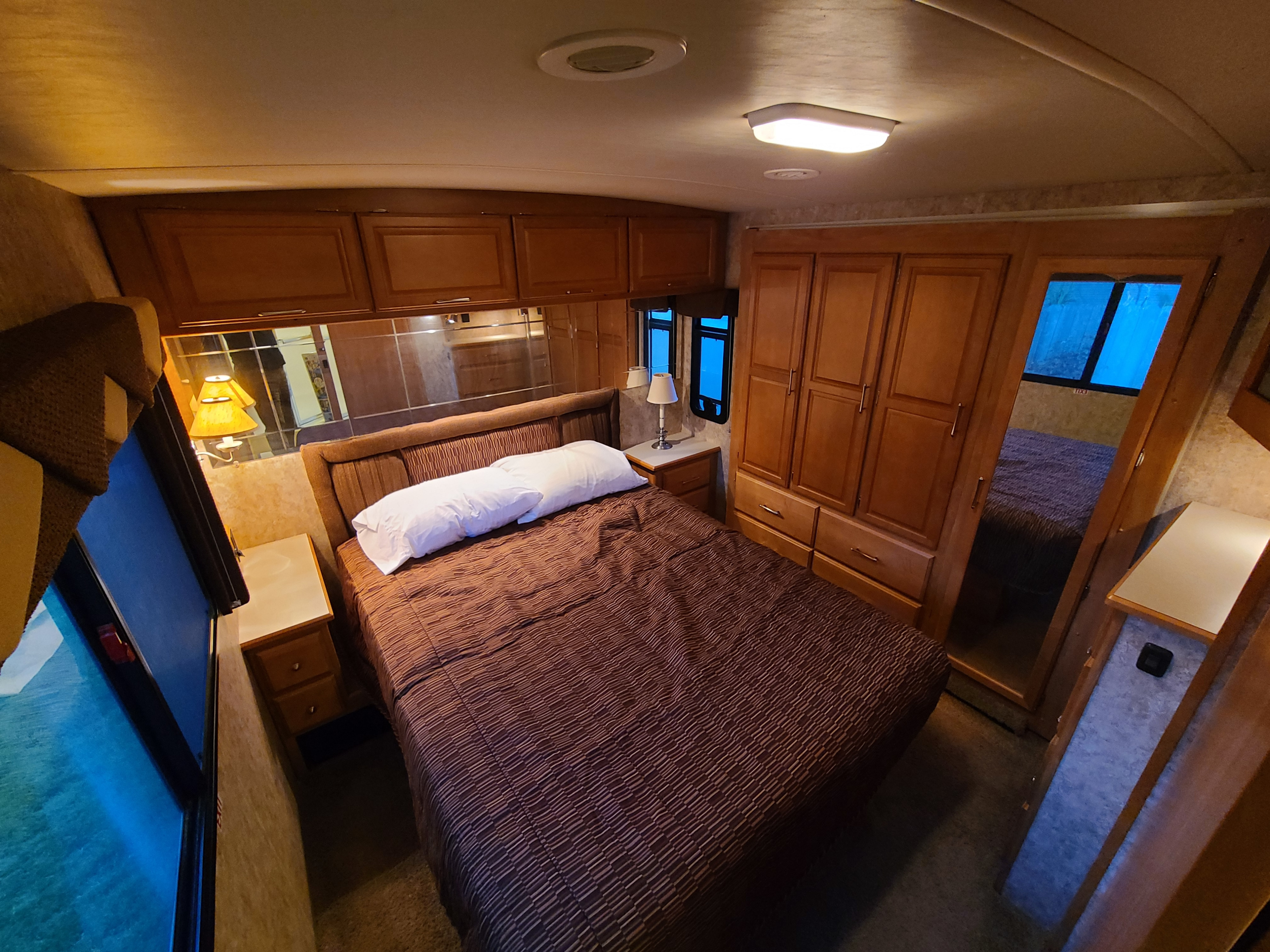 Spacious RV rental bedroom with comfy bed, brown comforter, ample wood cabinets, and large mirror wall.. Winnebago Journey 2006