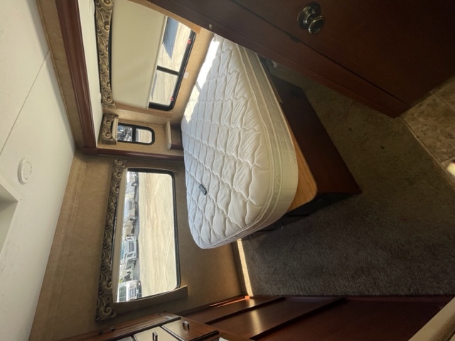 RV rental bedroom with white mattress, windows showing exterior, dark wood cabinetry, and carpeted floor.. Forest River Sunseeker 2015