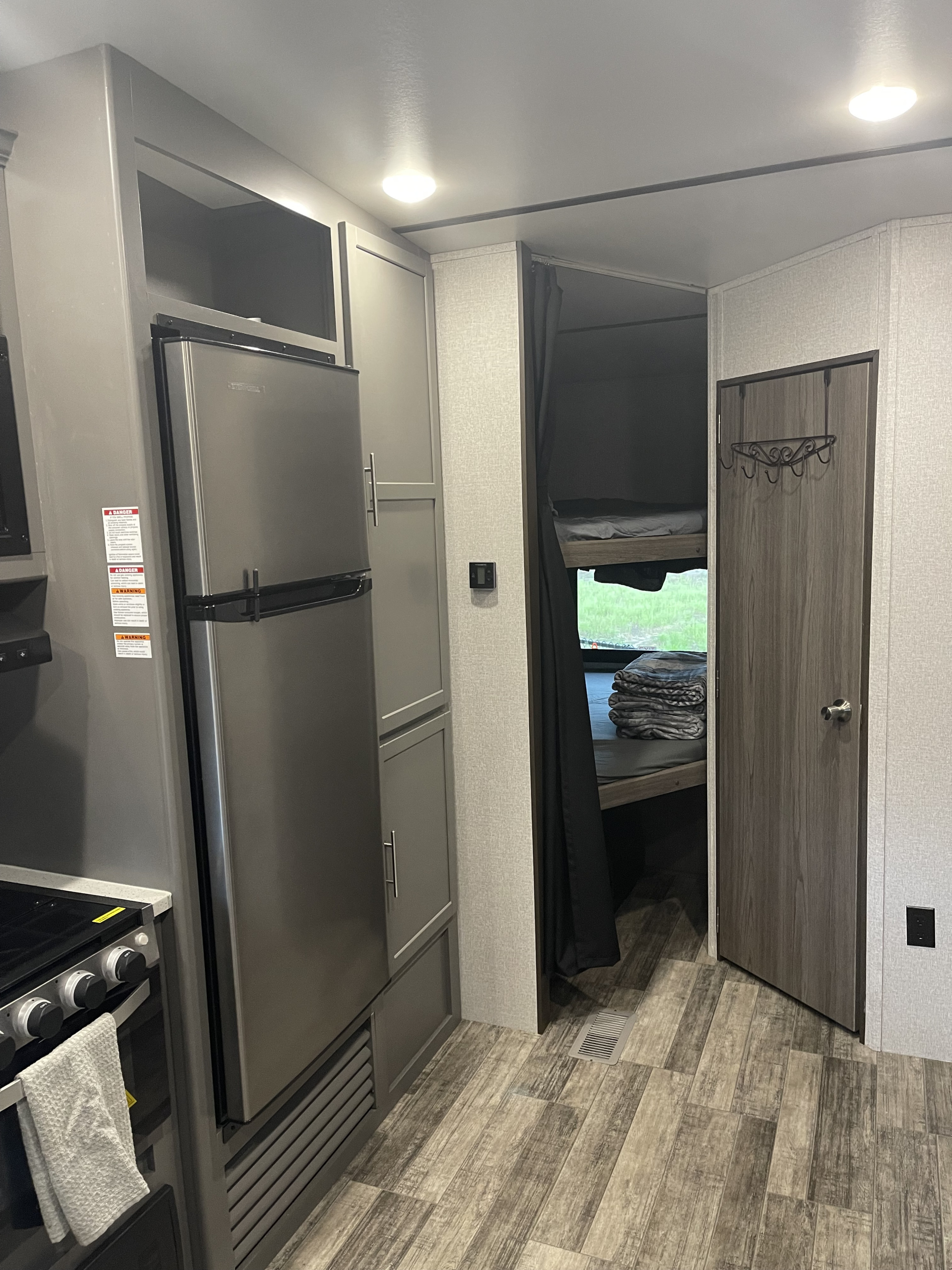 RV rental interior: compact kitchen with stainless steel fridge & stove, full cabinets, and bunk beds with a privacy curtain.. Crossroads RV Volante 2021