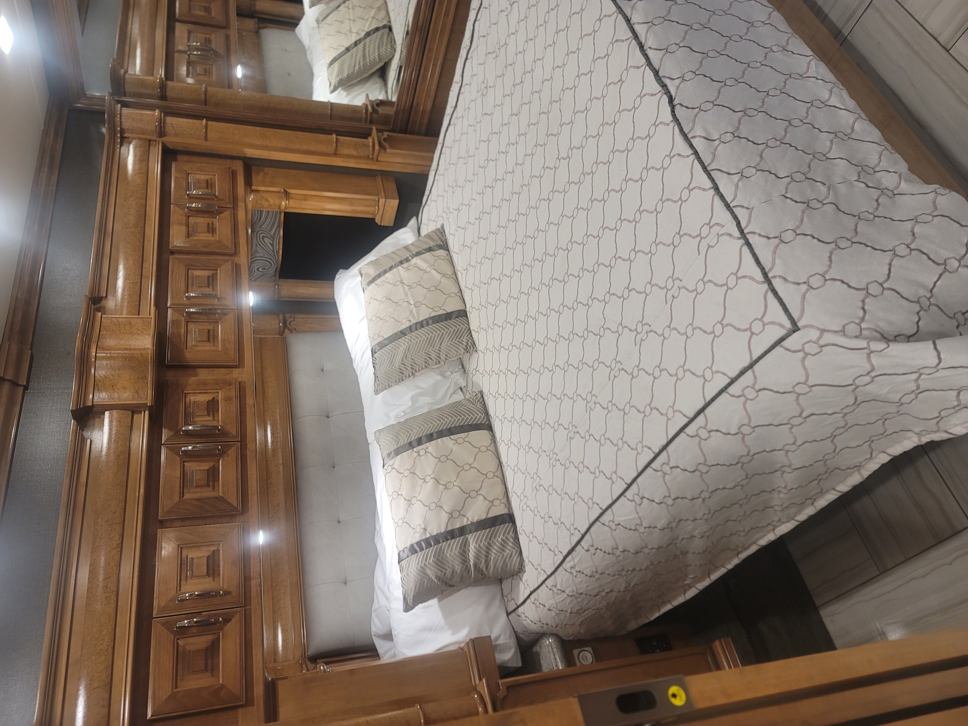 This RV rental showcases a lavish bedroom: comfortable bed, elegant tufted headboard, and ornate wooden cabinetry for premium travel.. American Coach 42B 2019