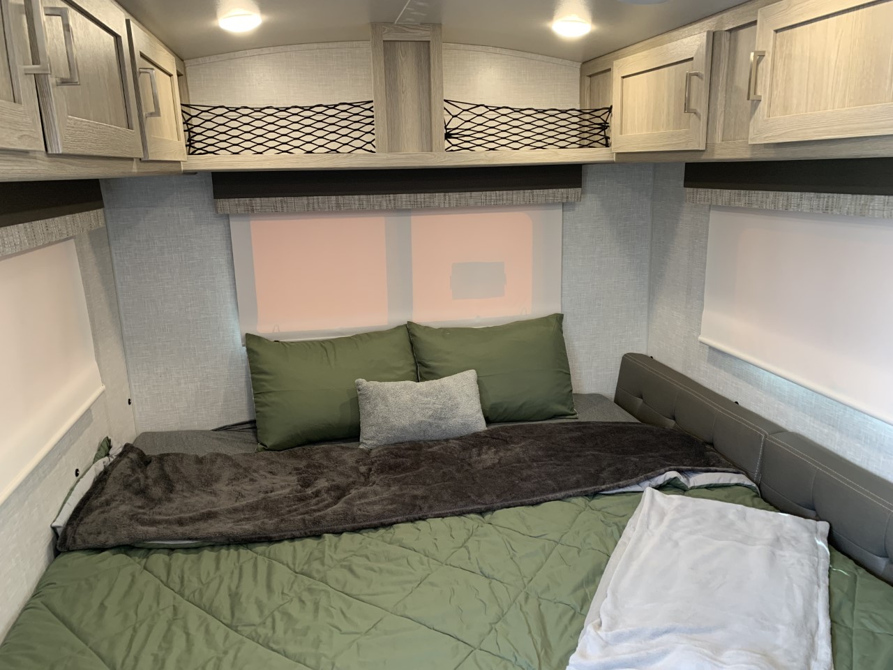 Cozy RV rental bedroom with green and grey bedding, overhead cabinets, and storage nets. Perfect for your next adventure.. Forest River Flagstaff E-Pro 2022