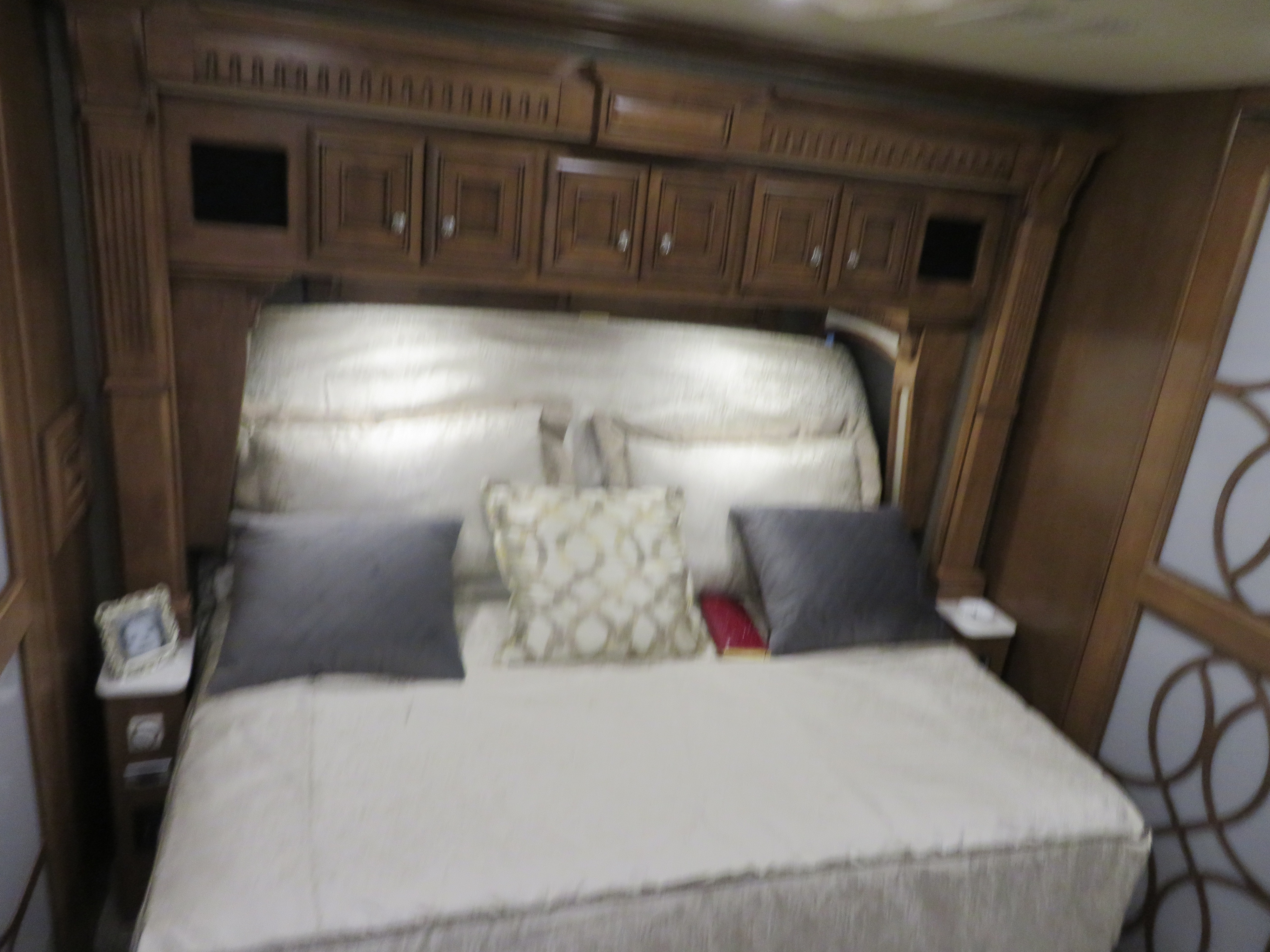 Comfortable RV rental bedroom featuring a large bed, decorative pillows, and ample wooden storage cabinets.. Monaco Signature 2019