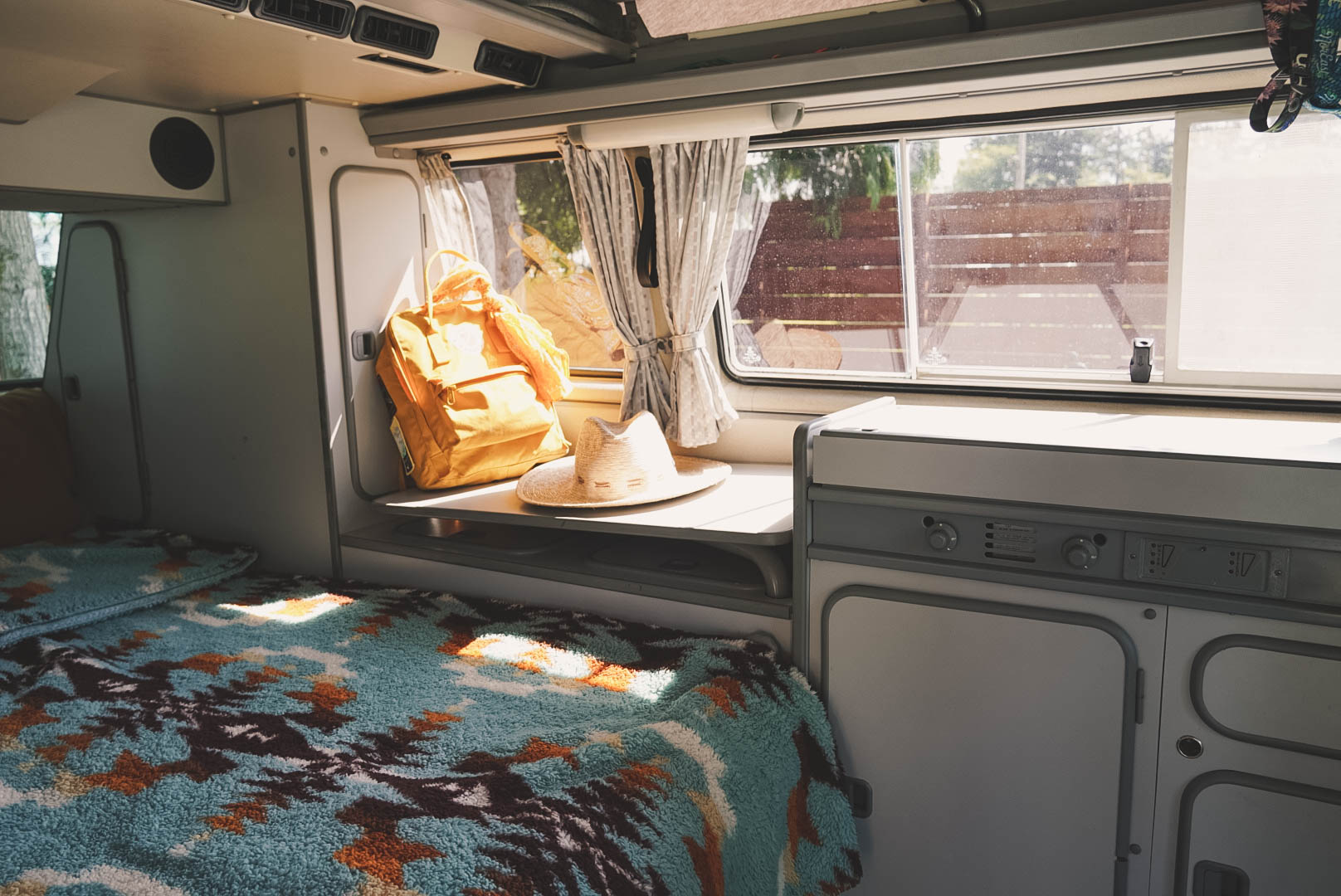 Cozy RV rental interior with a bed, sunlit window, and storage, perfect for travel adventures.. Volkswagen Westfalia 1987