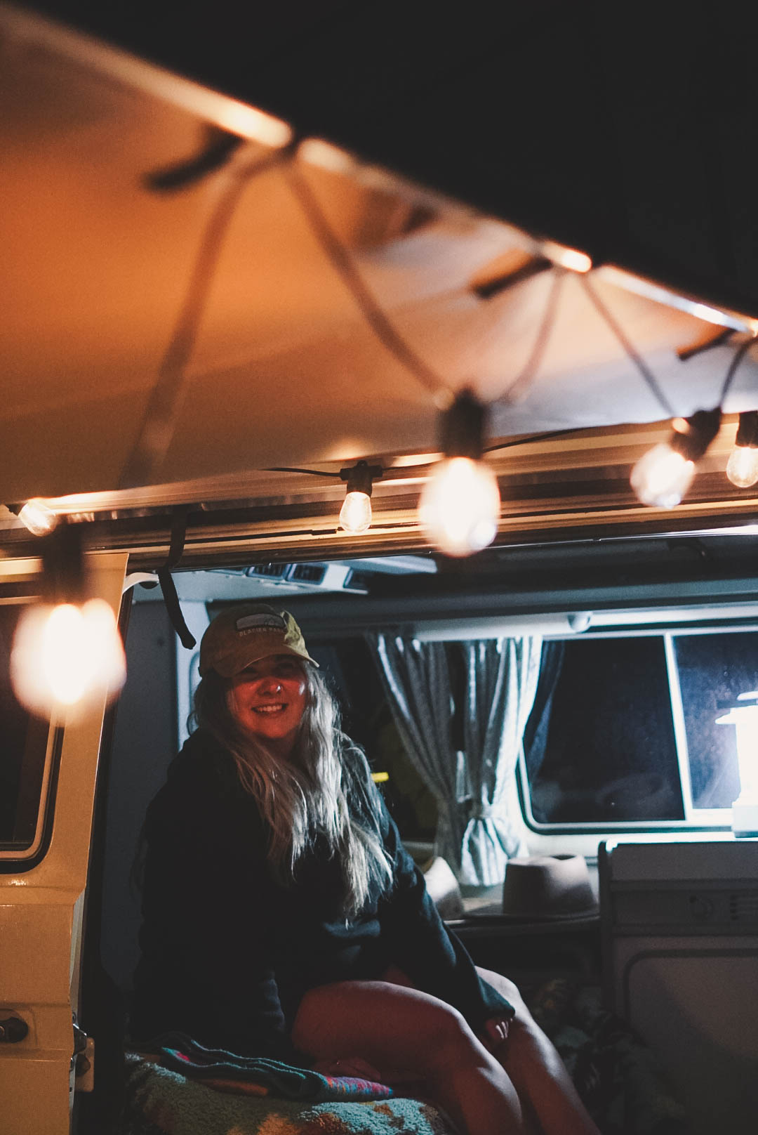 Cozy RV rental setup for van life adventure. Woman smiling inside a camper with warm string lights.. Volkswagen Westfalia 1987