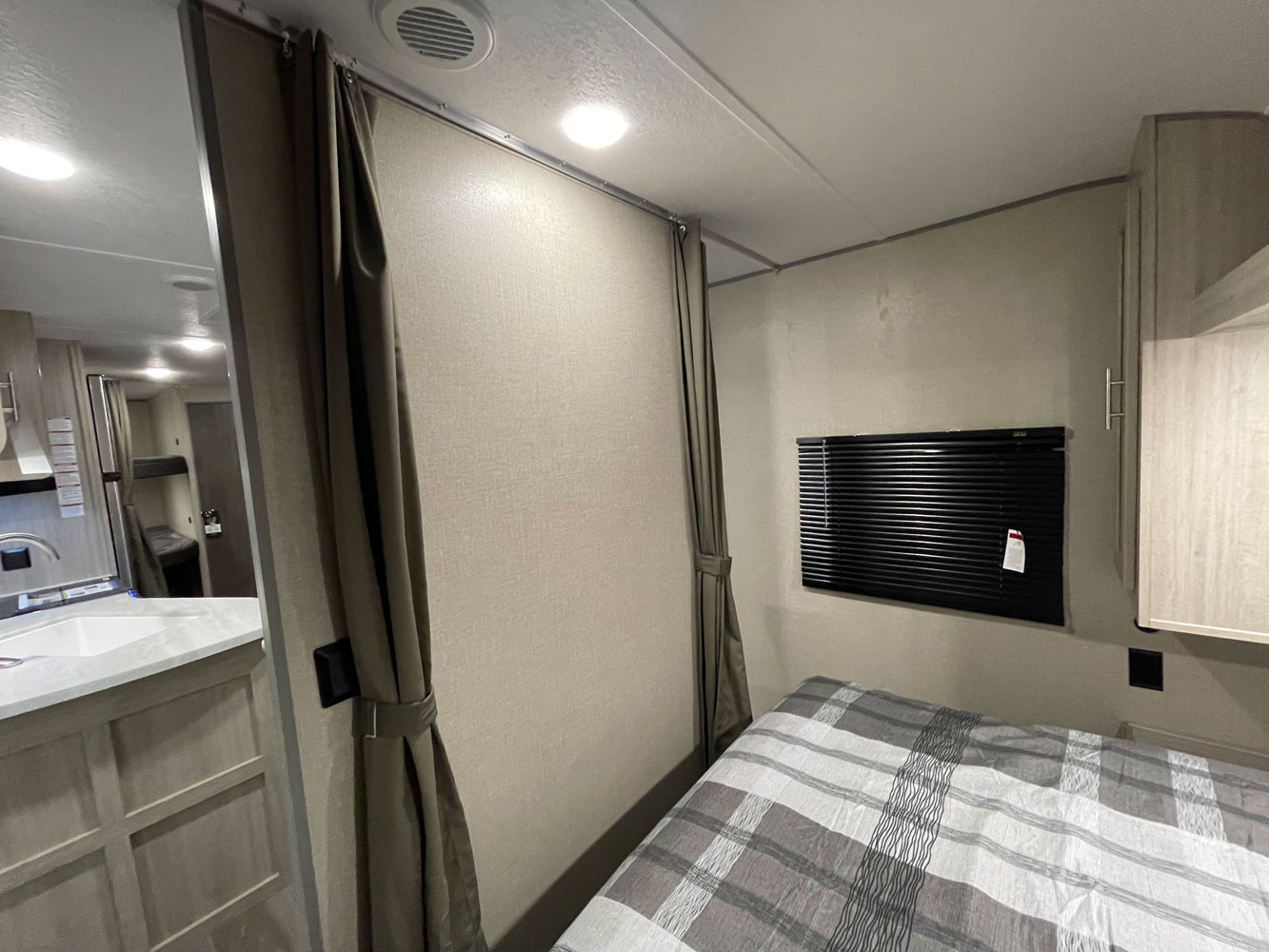 Cozy RV rental interior showing a private bedroom with curtain partition, a window, and adjacent kitchen area.. Coachmen Catalina 2023