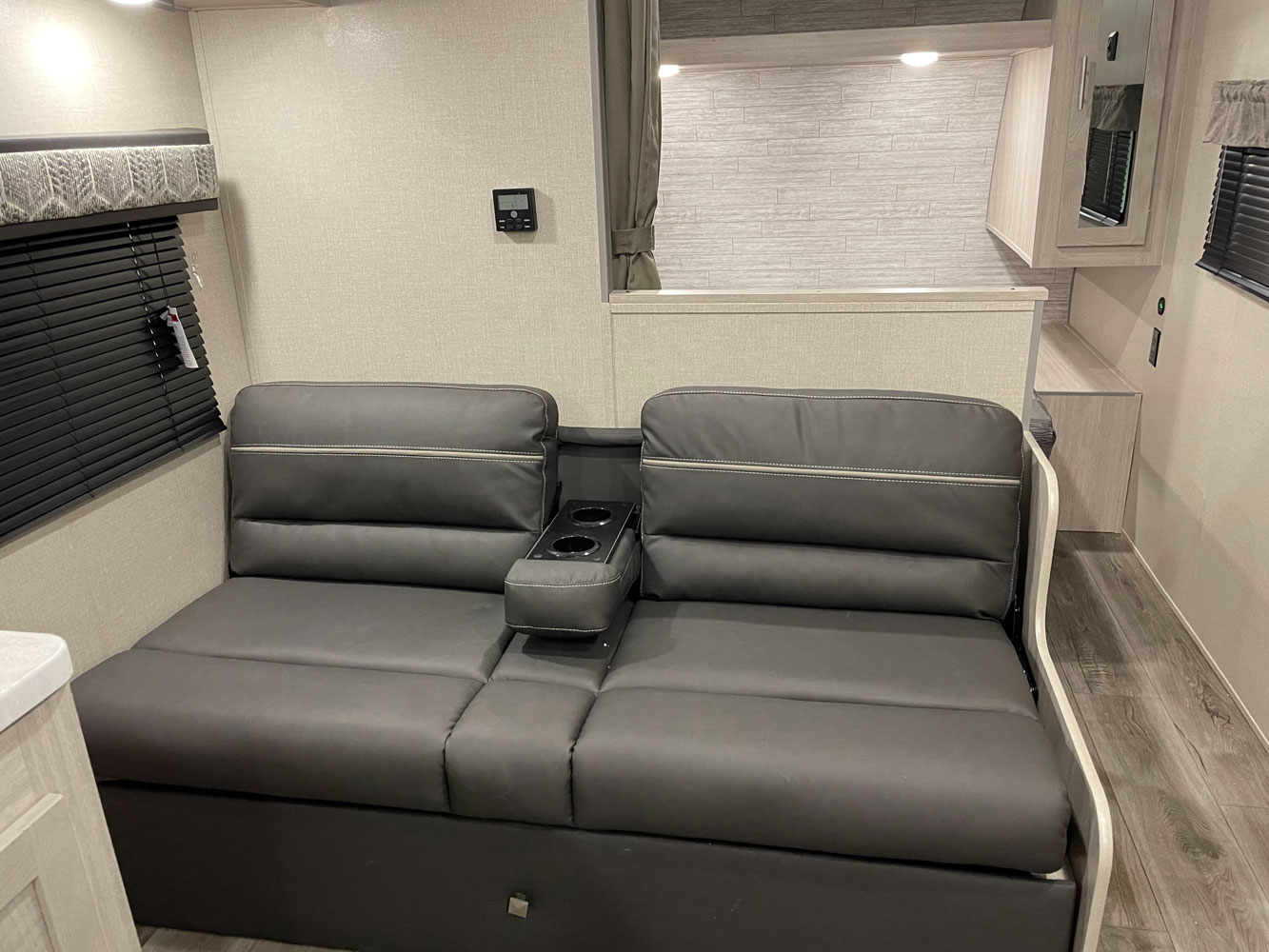 Modern RV rental interior with a gray convertible sofa, cup holders, and light wood cabinetry. Great for travel.. Coachmen Catalina 2023