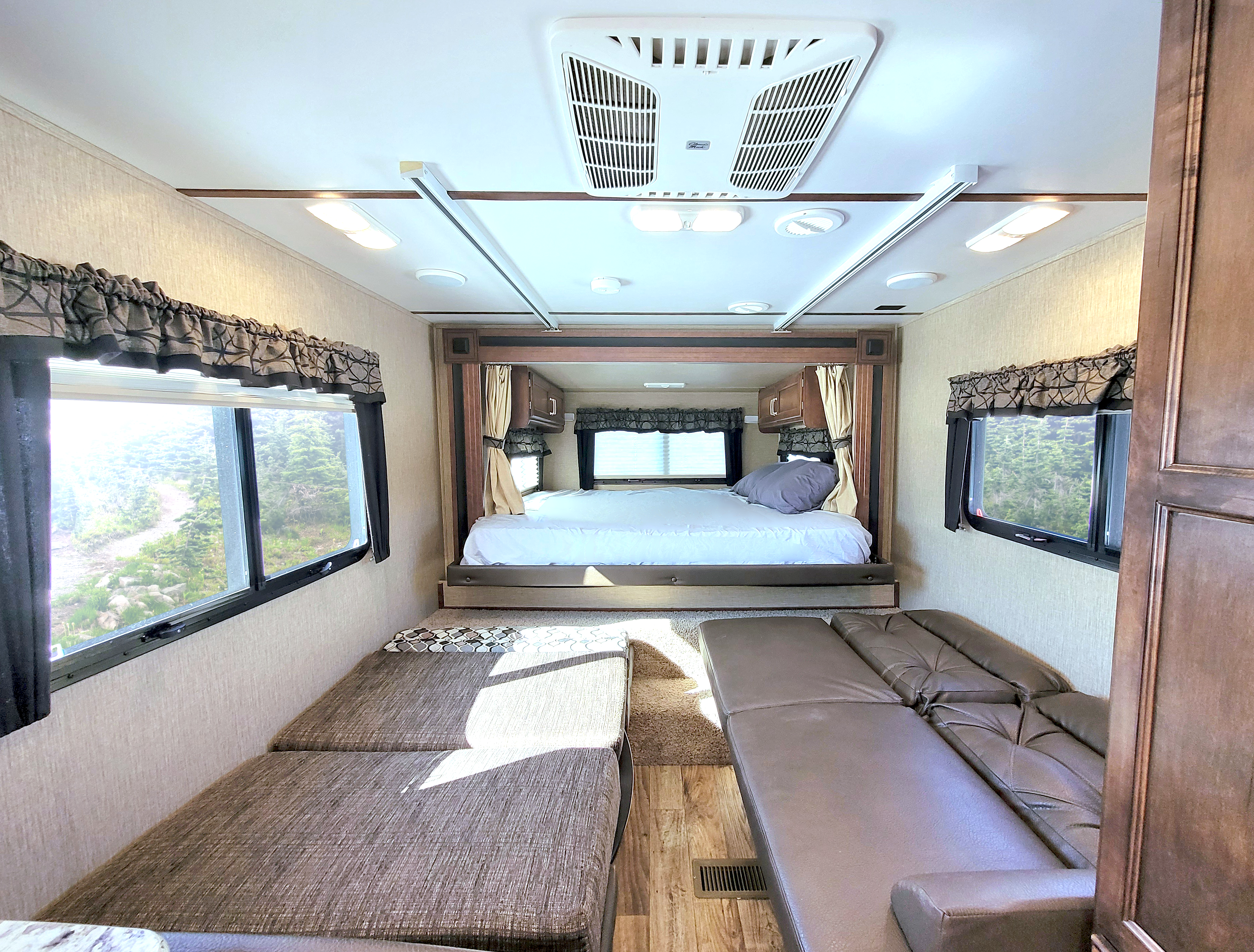 This inviting RV rental interior features a comfortable bed, lounge seating, and large windows revealing a forest path.. Keystone Outback 2018