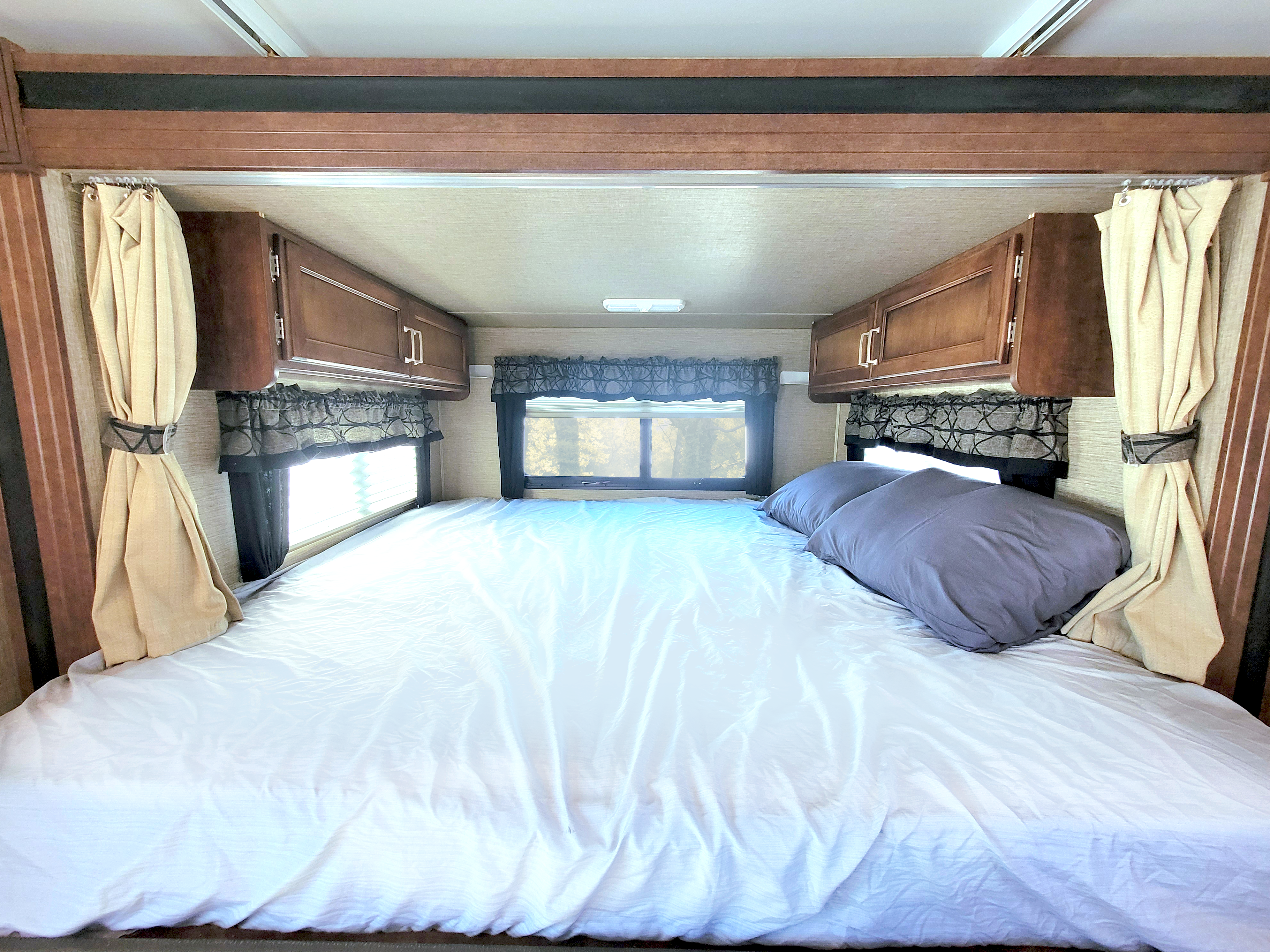 Cozy RV rental bedroom: Features a large bed with white sheets, two grey pillows, windows, and wood cabinets.. Keystone Outback 2018