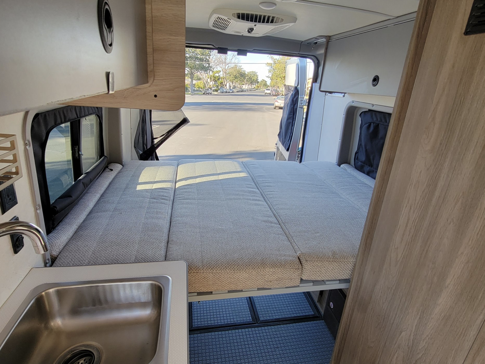 Cozy RV rental interior shows a bed, sink, storage, and open back doors revealing a street view.. Winnebago Solis 59PX 2021
