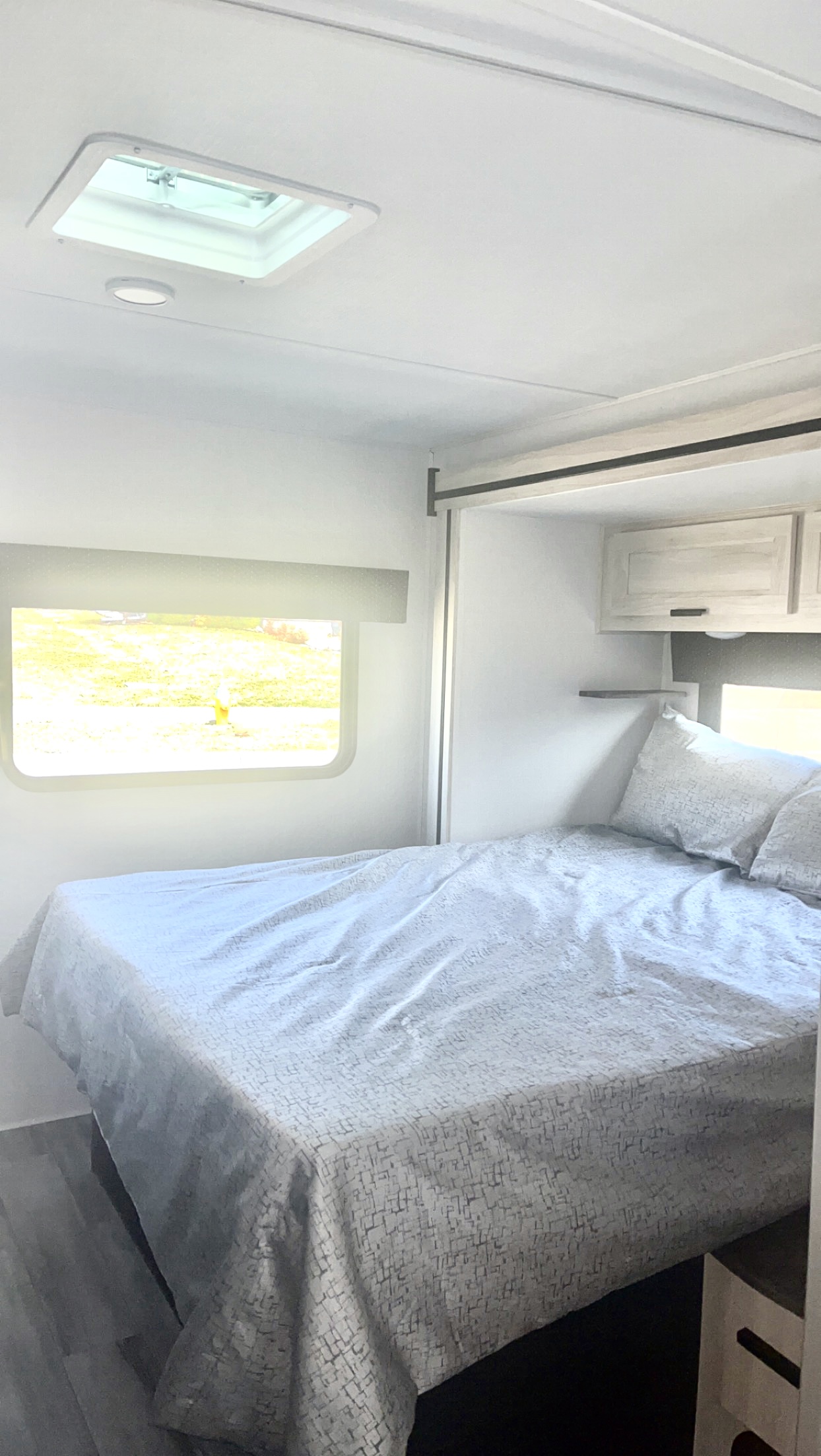 Bright, modern RV rental bedroom: Features a bed with patterned comforter, window view, overhead cabinets, and ceiling vent.. Forest River Forester 2023
