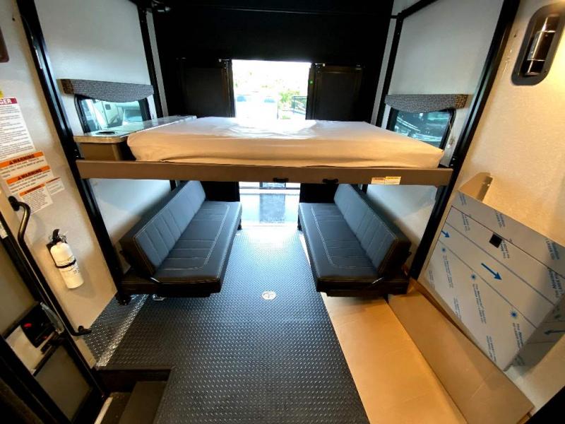 RV rental: Toy hauler garage with an upper bunk bed and two lower convertible benches on a diamond plate floor, rear door open.. Thor Motor Coach Outlaw 2023
