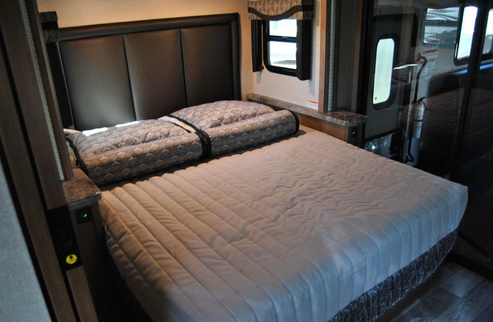 This RV rental bedroom features a comfortable bed, stylish headboard, and window, providing a cozy sleeping area.. Thor Motor Coach Outlaw 2023