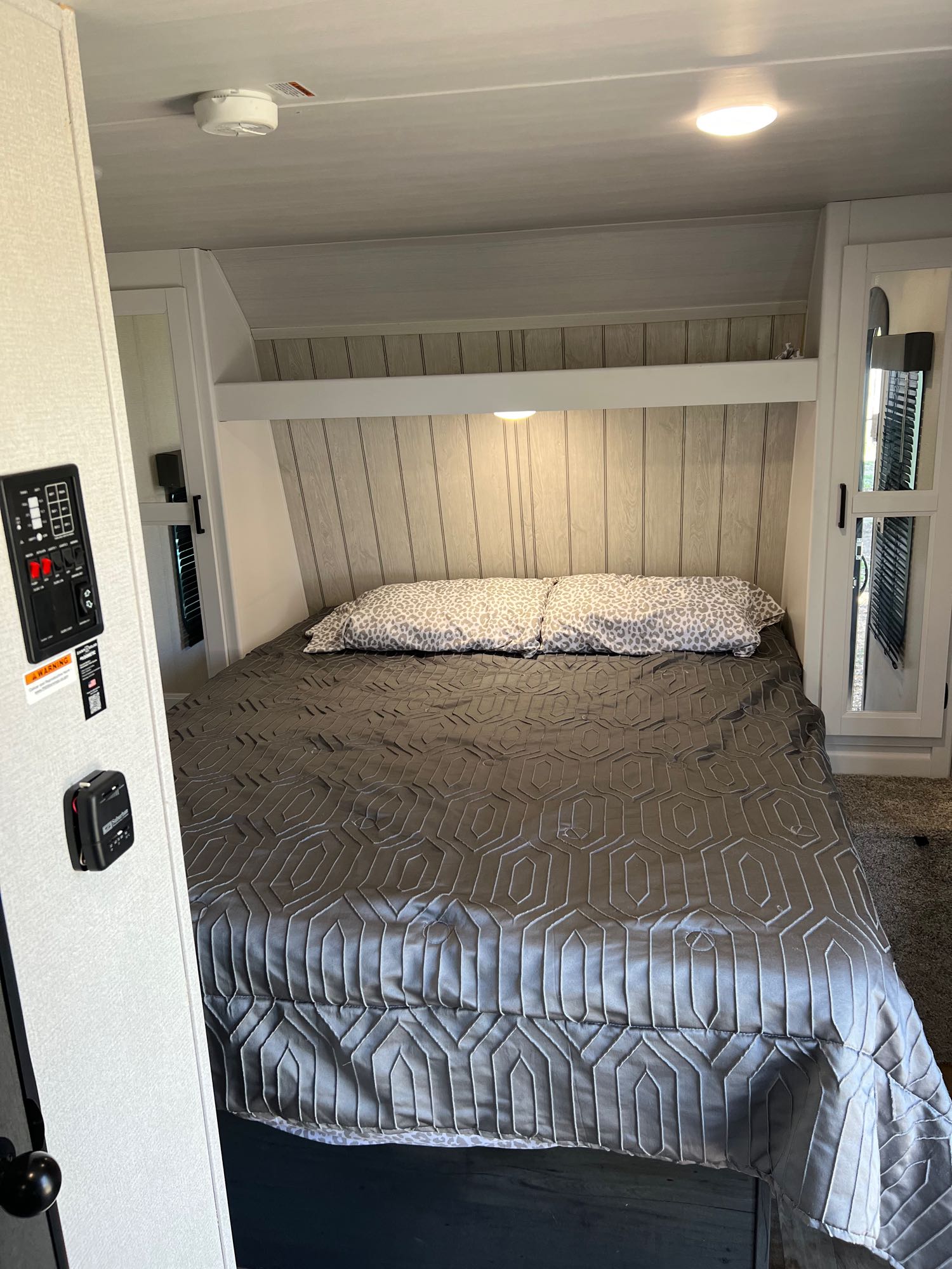 RV rental bedroom with a comfortable bed, gray geometric comforter, leopard pillows, and easy-access control panel.. Keystone Hideout 2022