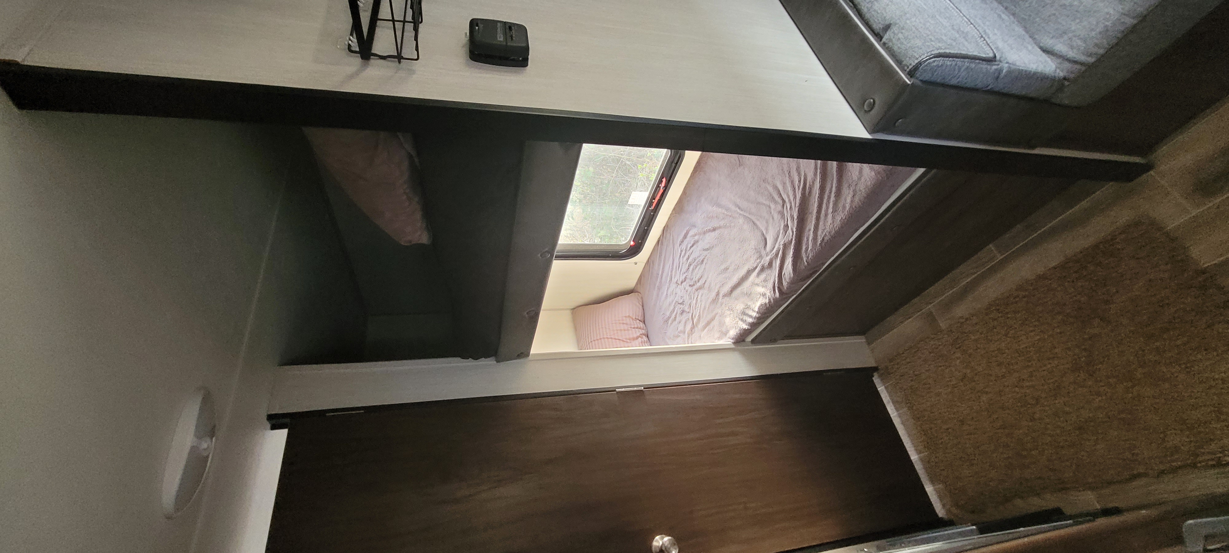 RV rental interior. Two bunk-style sleeping areas, one with bedding and a window, the other a darker storage alcove.. Forest River Cascade 2019