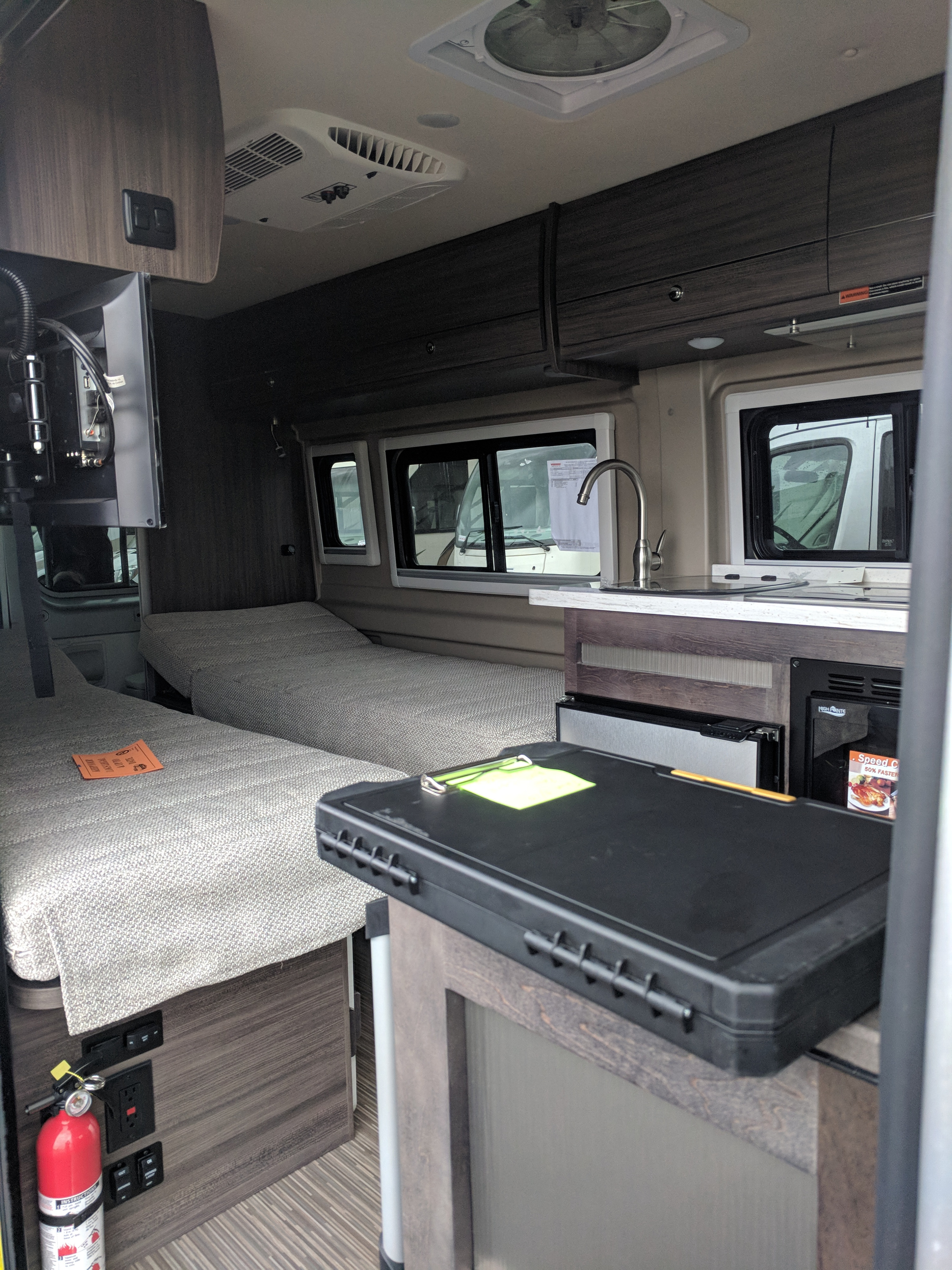 Spacious RV rental interior with two beds, a kitchen with sink, and overhead storage. Ideal for road trip comfort.. Winnebago Travato 2019
