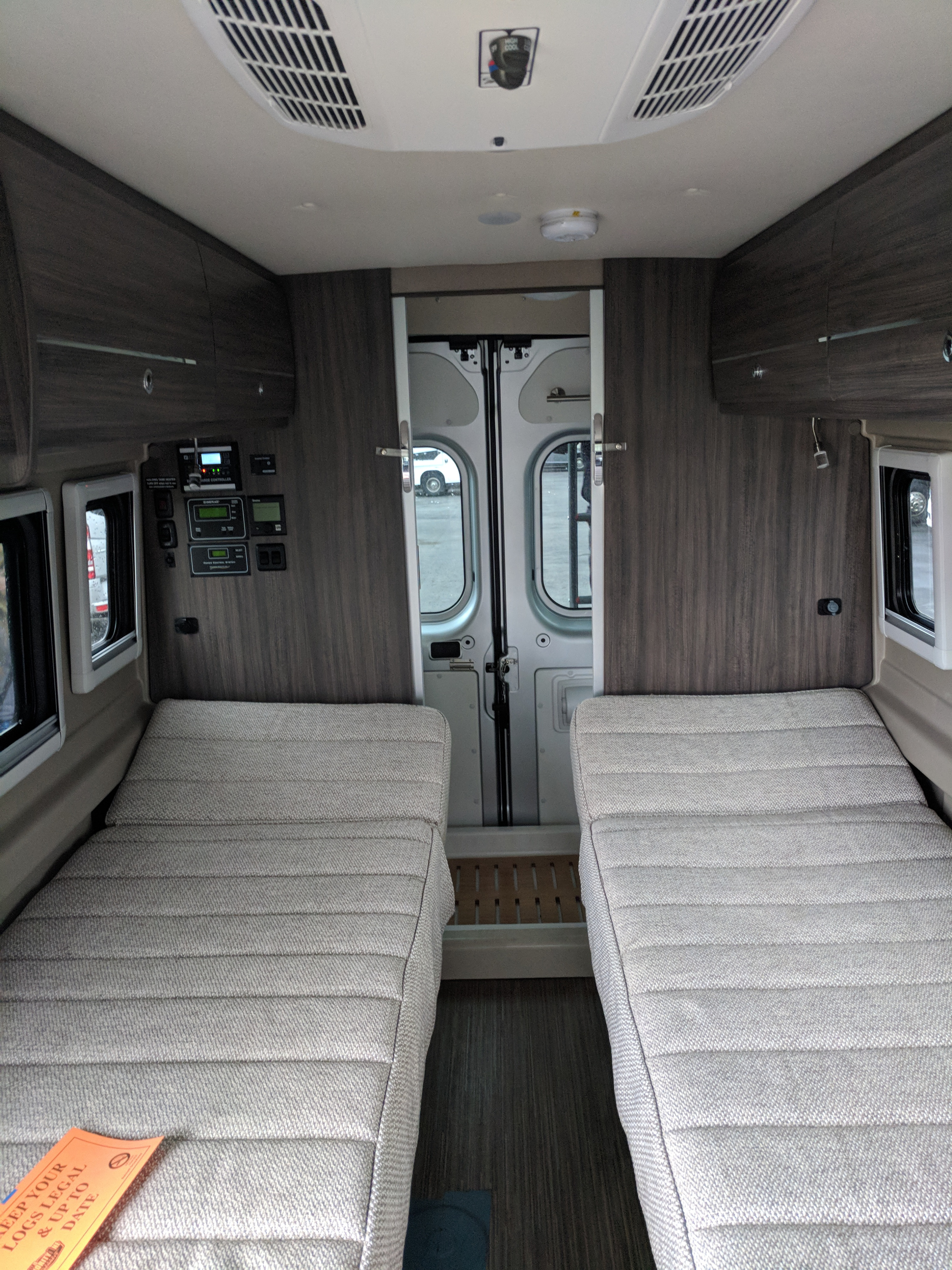 The cozy interior of an RV rental, featuring two single beds, built-in cabinetry, and system controls for easy living on the road.. Winnebago Travato 2019