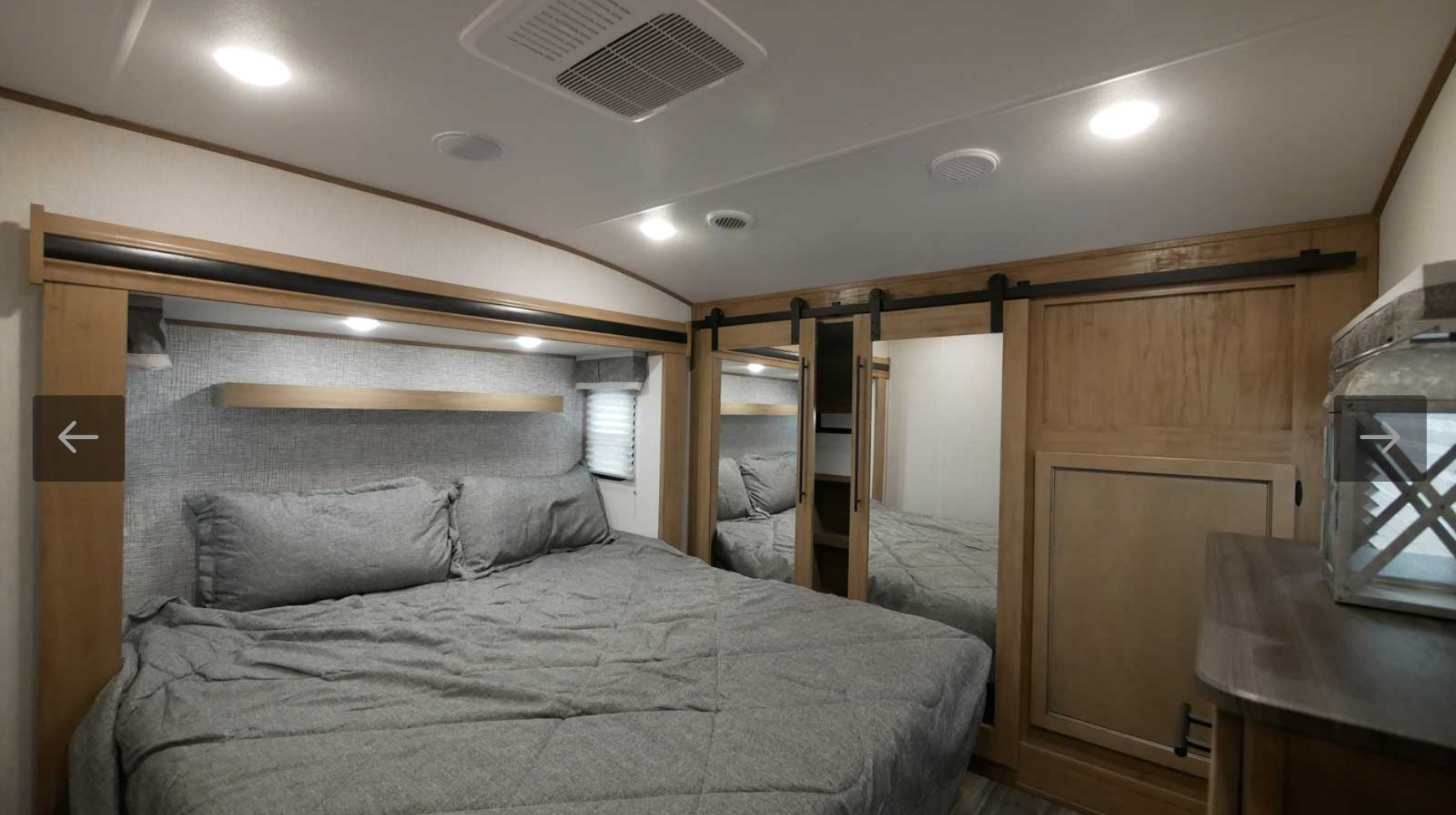 Cozy RV rental bedroom features gray bedding, a wooden headboard shelf, mirrored sliding closet doors, and overhead AC.. Forest River Sabre 2021