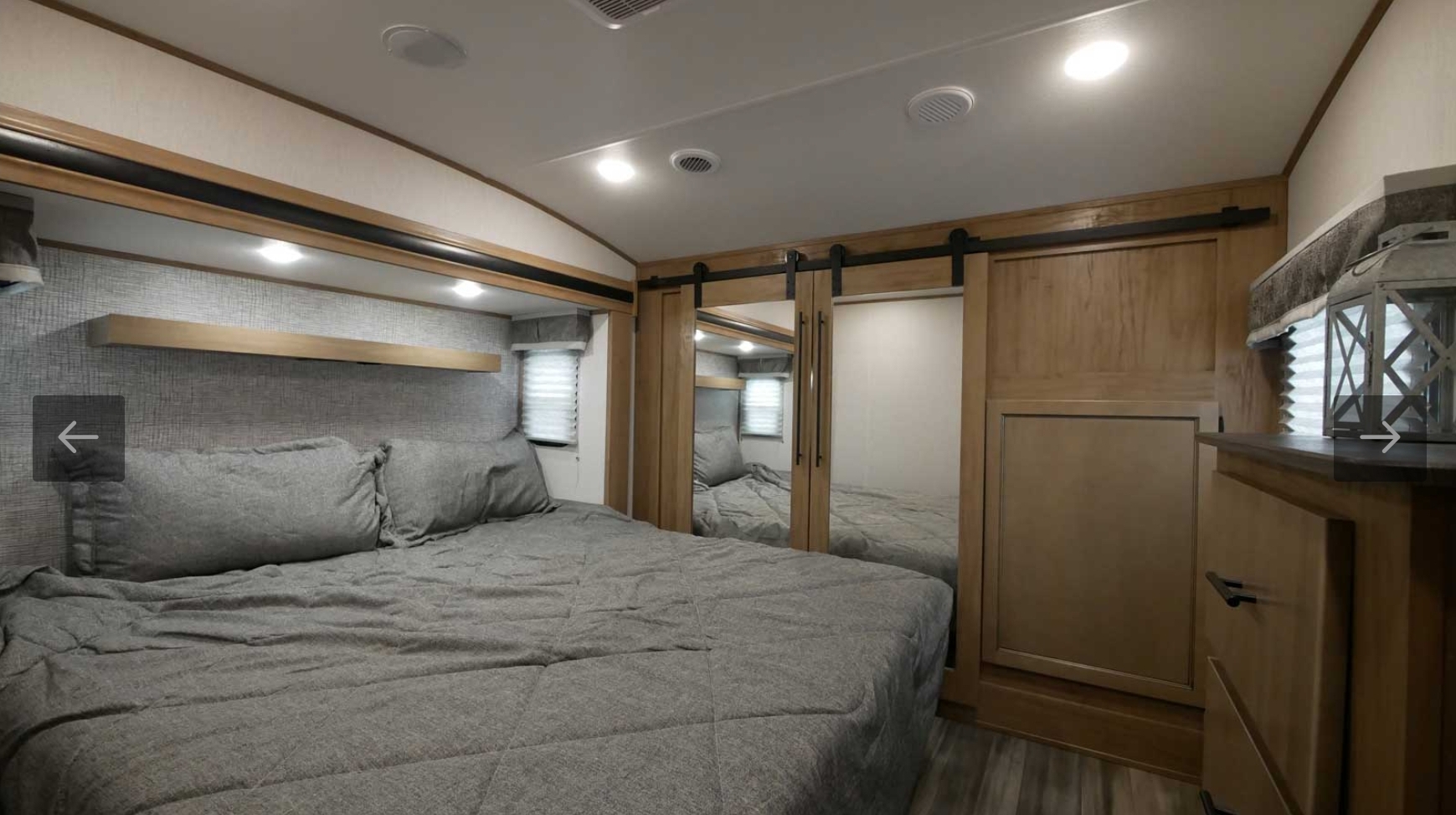 Serene RV rental bedroom featuring a cozy gray bed, floating shelf, mirrored barn doors, and wood cabinetry.. Forest River Sabre 2021