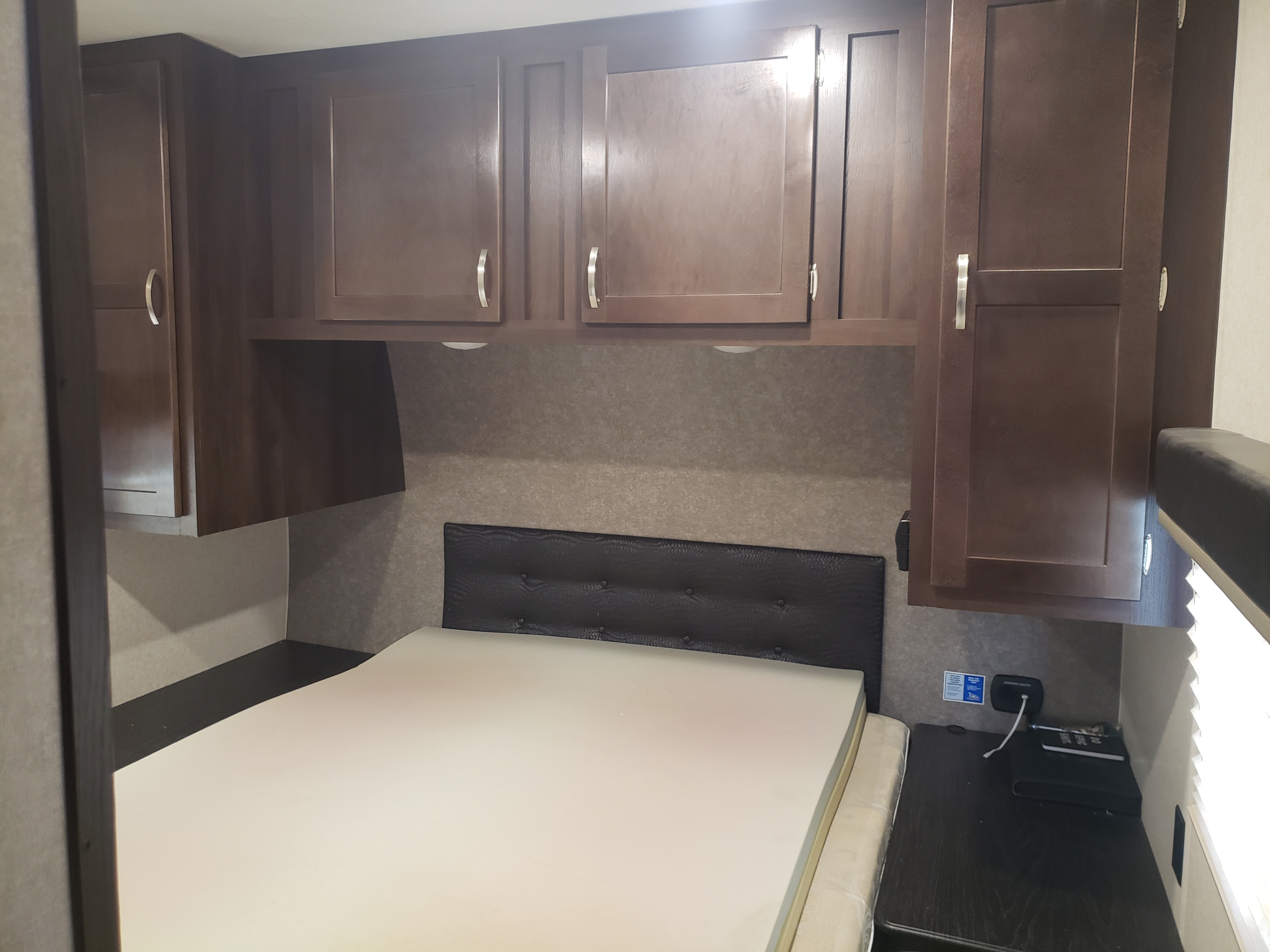 Cozy RV rental bedroom with dark wood cabinets, a tufted headboard, and bedside charging.. Jayco Octane 2019