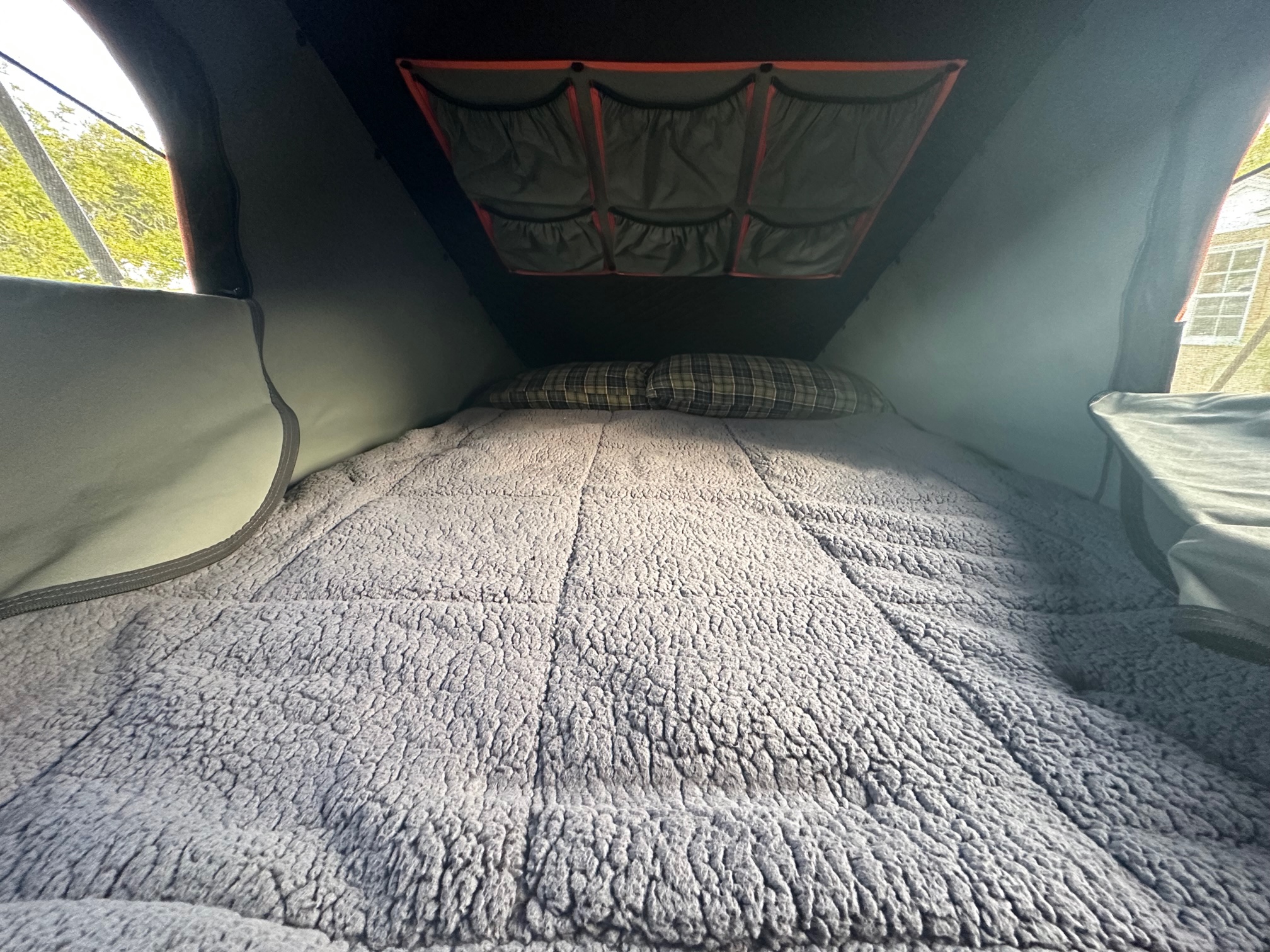 An RV rental's comfy interior: a bed with a plush blanket & plaid pillows, and ceiling storage pockets visible.. toyota Tacoma TRD Off-Road 2017