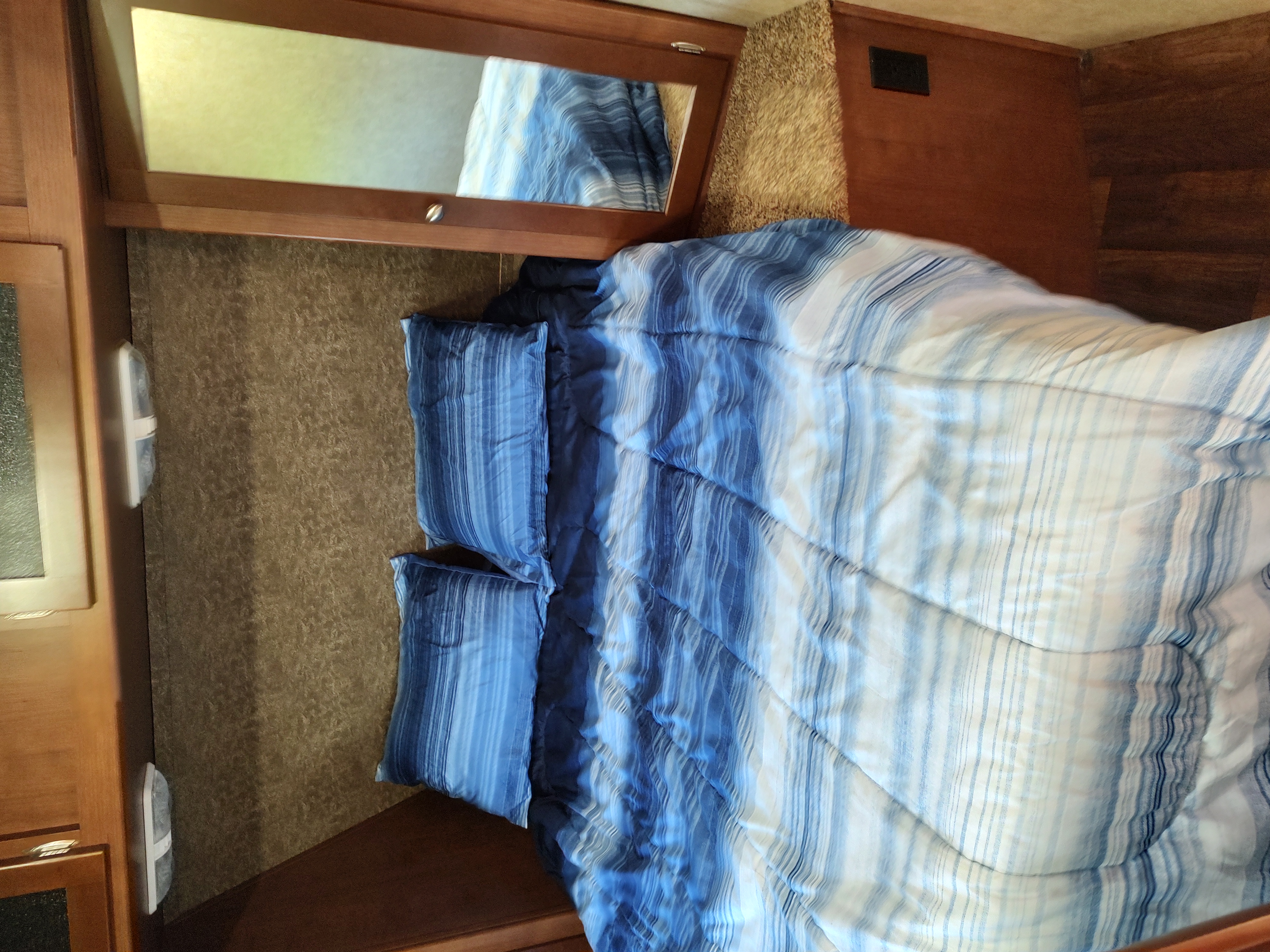 This RV rental bedroom features a comfy bed with blue and white striped bedding, two pillows, and surrounding wooden cabinetry.. Dutchmen Kodiak 2014