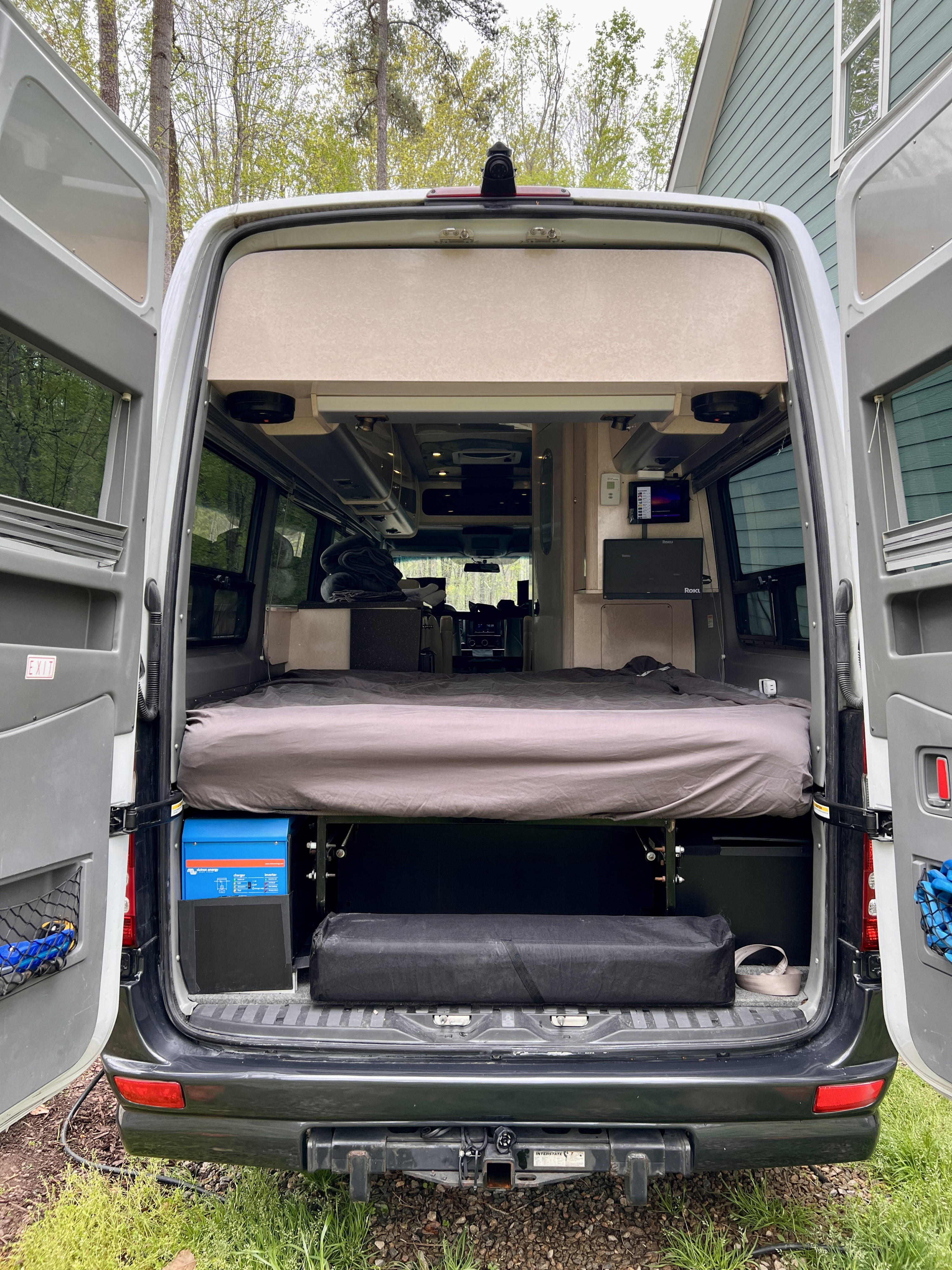 Spacious RV rental interior from the rear: bed, power system, and storage with open back doors.. Airstream Interstate 2010