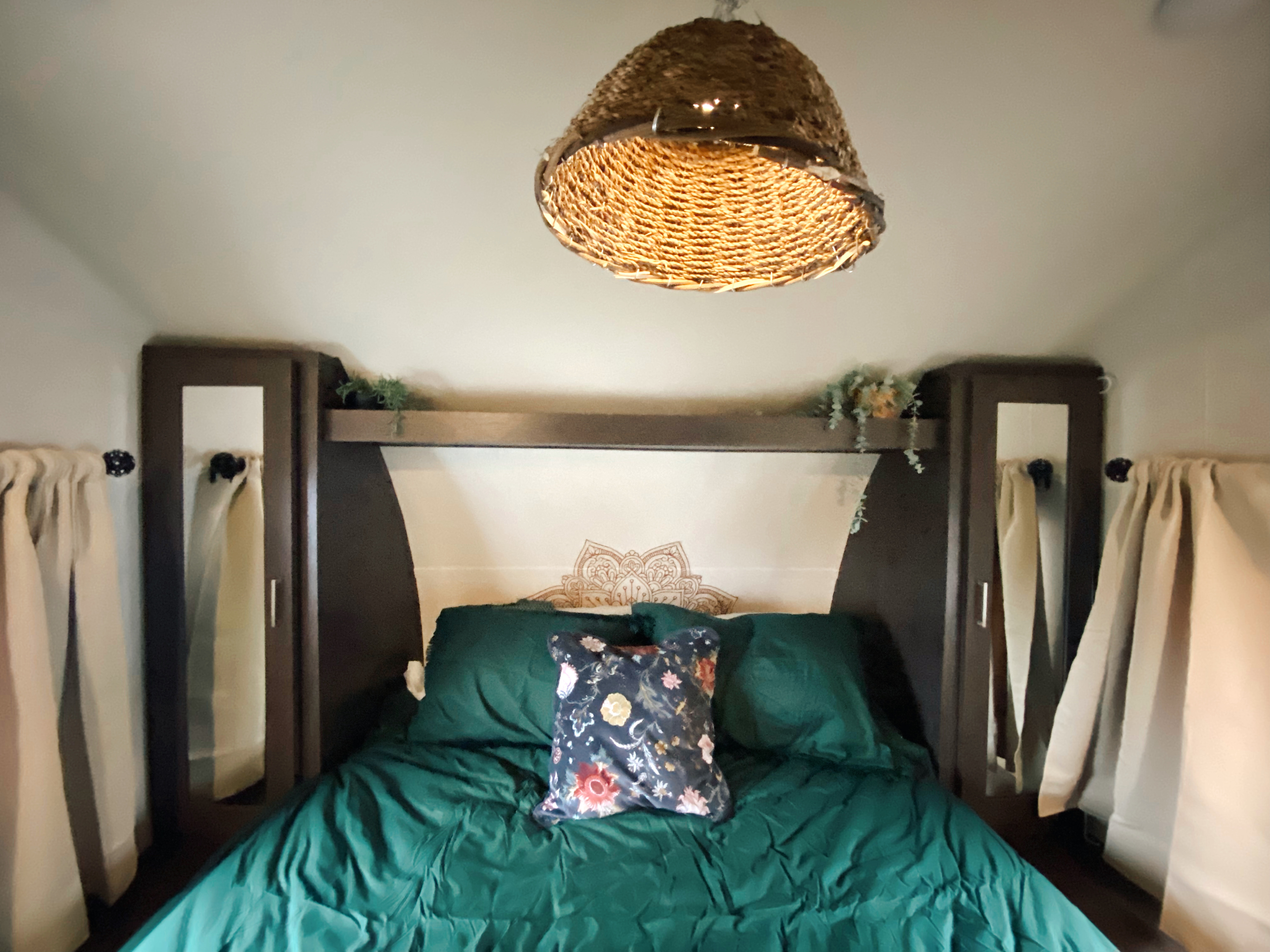 Cozy RV rental bedroom with dark green bedding, floral pillow, and wicker light. Perfect glamping.. Forest River Wildwood X-Lite 2019