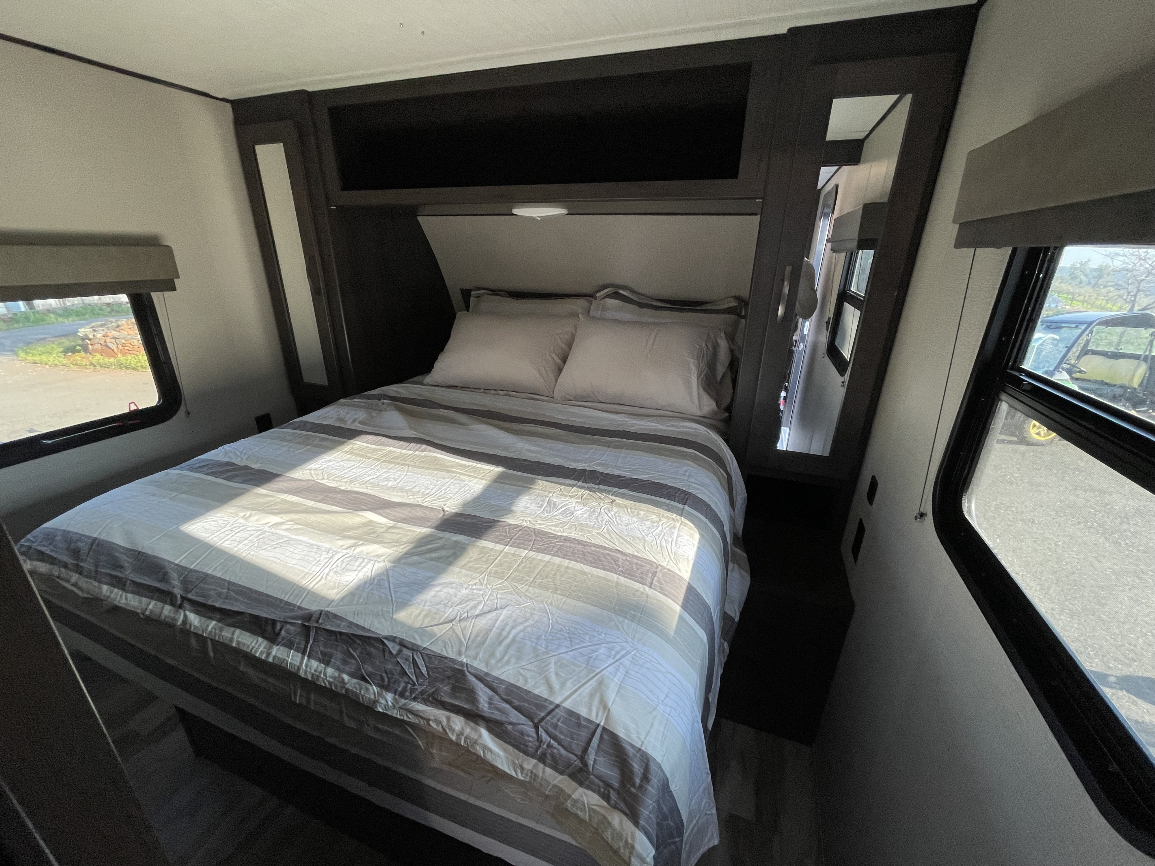 Cozy RV rental bedroom with striped bedding, built-in storage, and bright windows offering outdoor views.. Grand Design Transcend Xplor 2020