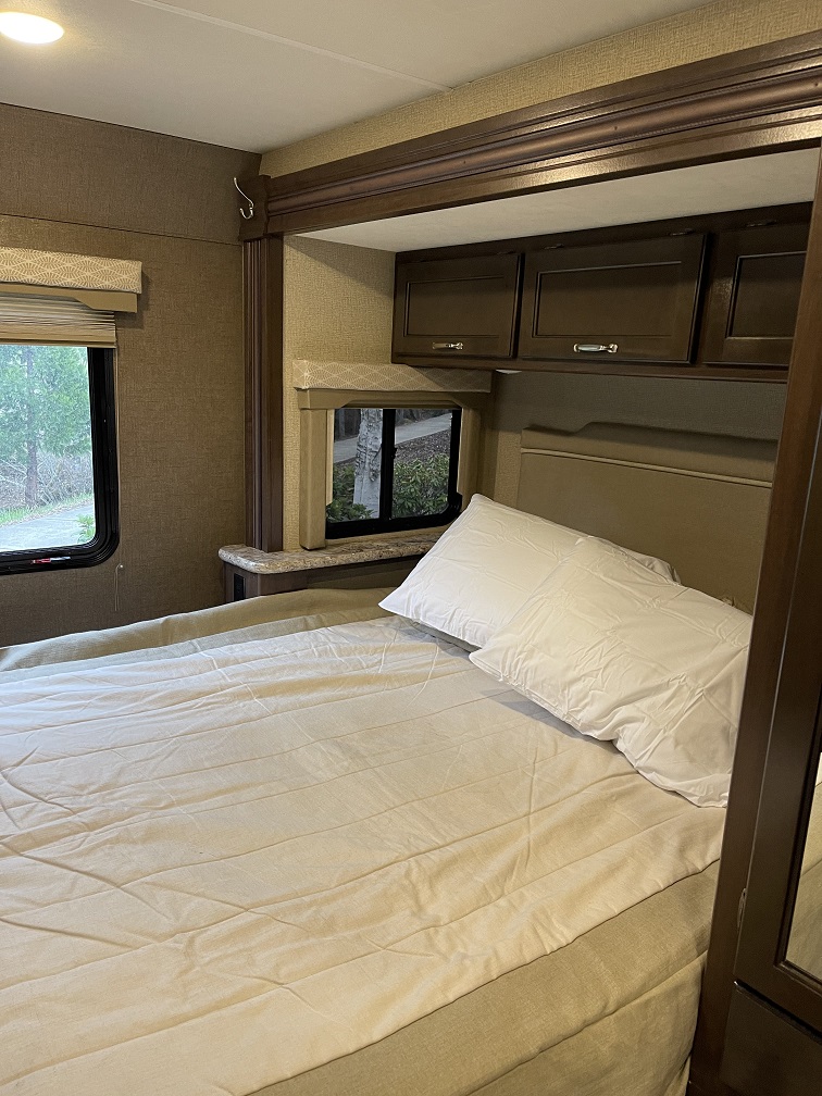 An RV rental bedroom: cozy space with a made bed, windows, and practical overhead storage cabinets.. Thor Freedom Elite 2019