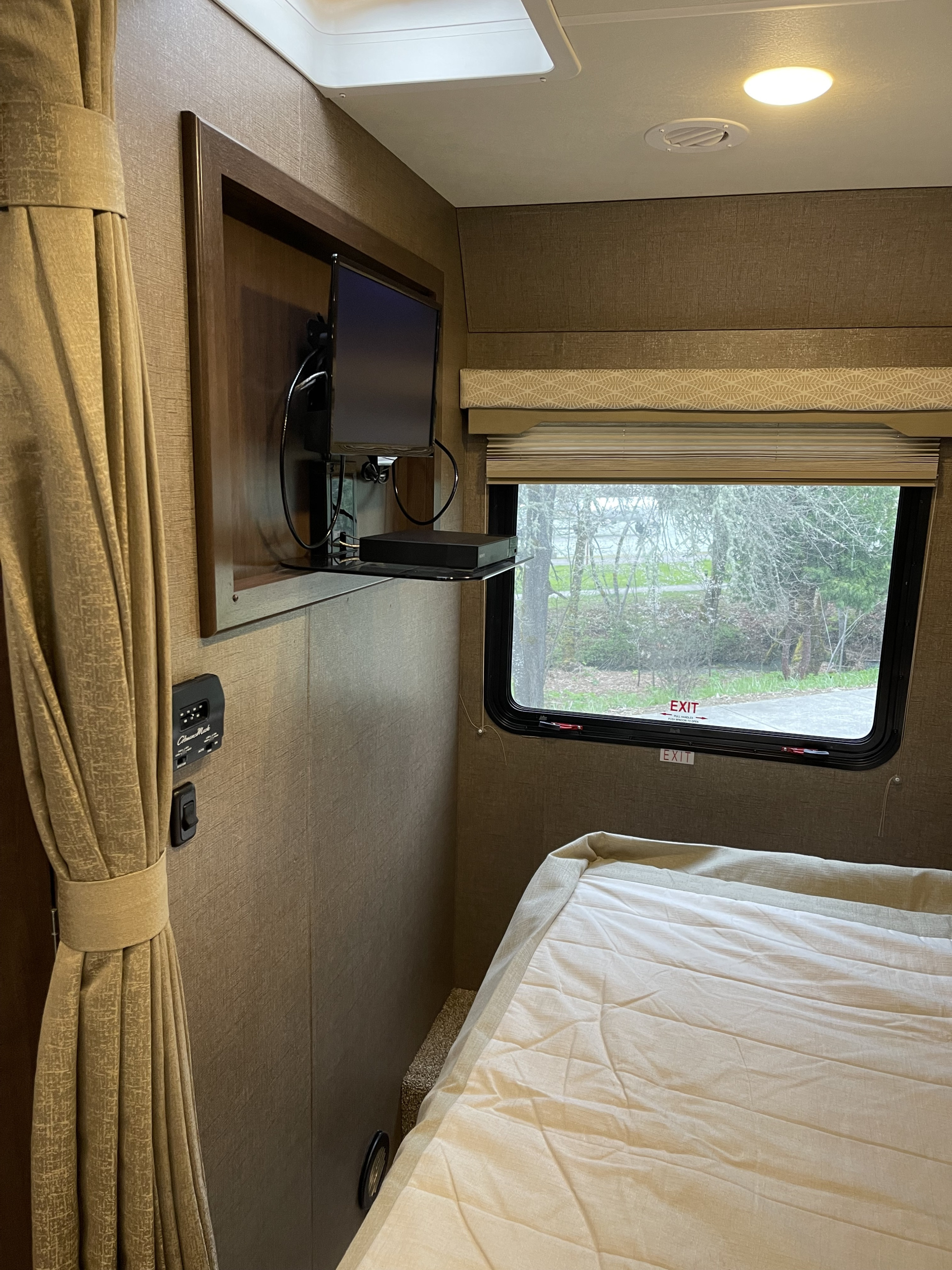 Inside an **rv rental**: a compact bedroom with TV, a comfortable bed, and window with park view.. Thor Freedom Elite 2019