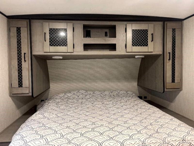 Cozy RV rental bedroom featuring a patterned bed, overhead cabinets, and side storage for comfort.. Heartland RVs Mallard 2022