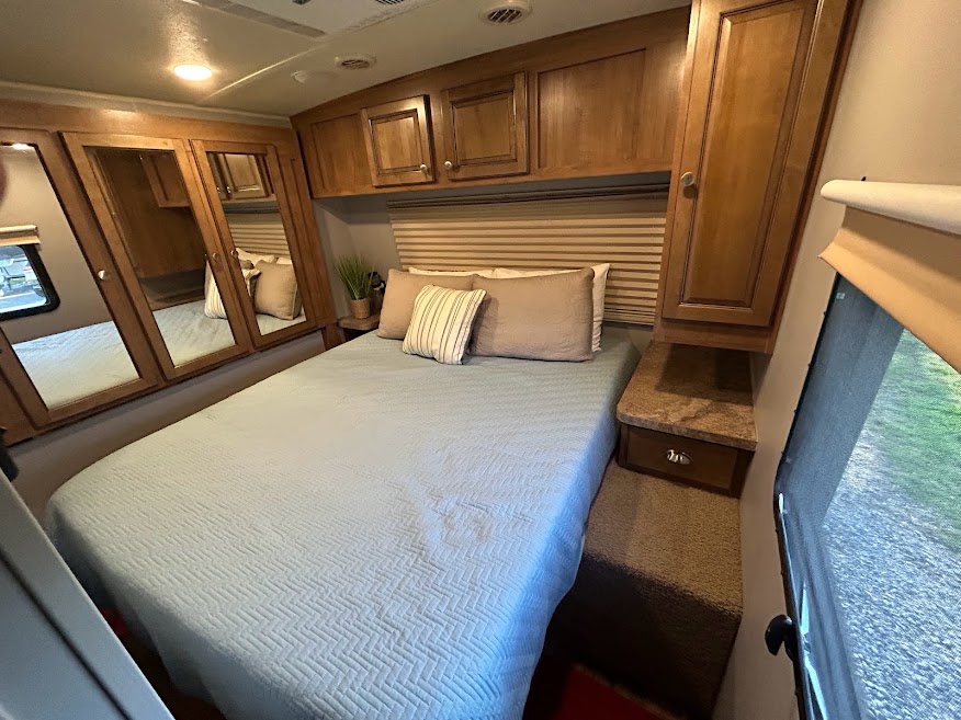 Comfortable bedroom in an RV rental, featuring a large bed, wooden overhead cabinets, and mirrored closet doors.. Forest River Rockwood Signature Ultra Lite 2017