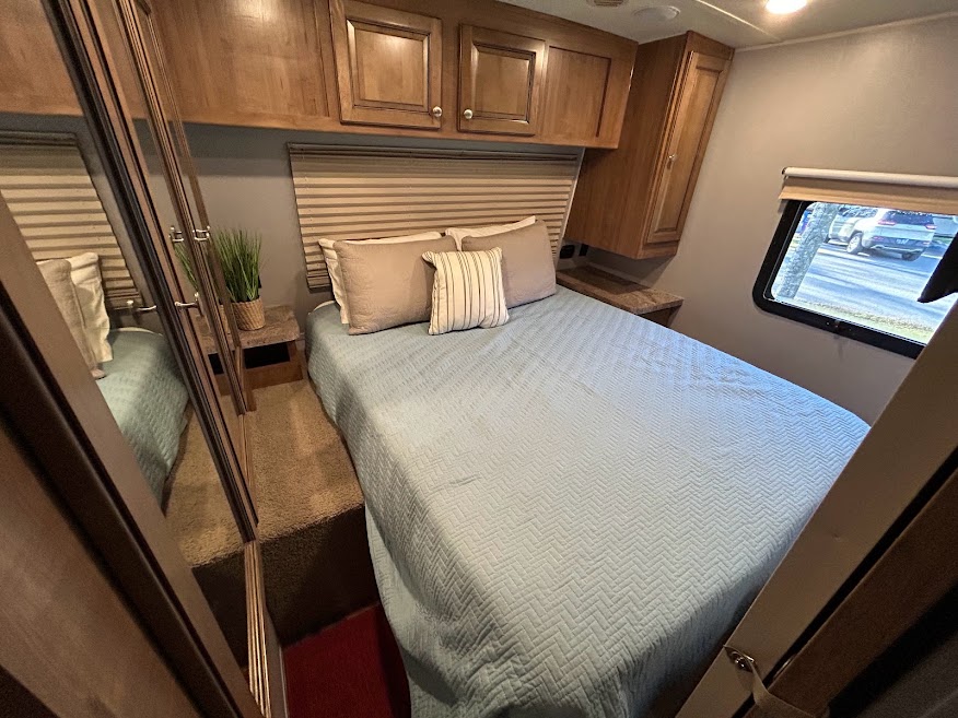 Cozy RV rental bedroom featuring a light blue bed, overhead cabinets, and a mirrored wardrobe, perfect for comfortable travel.. Forest River Rockwood Signature Ultra Lite 2017