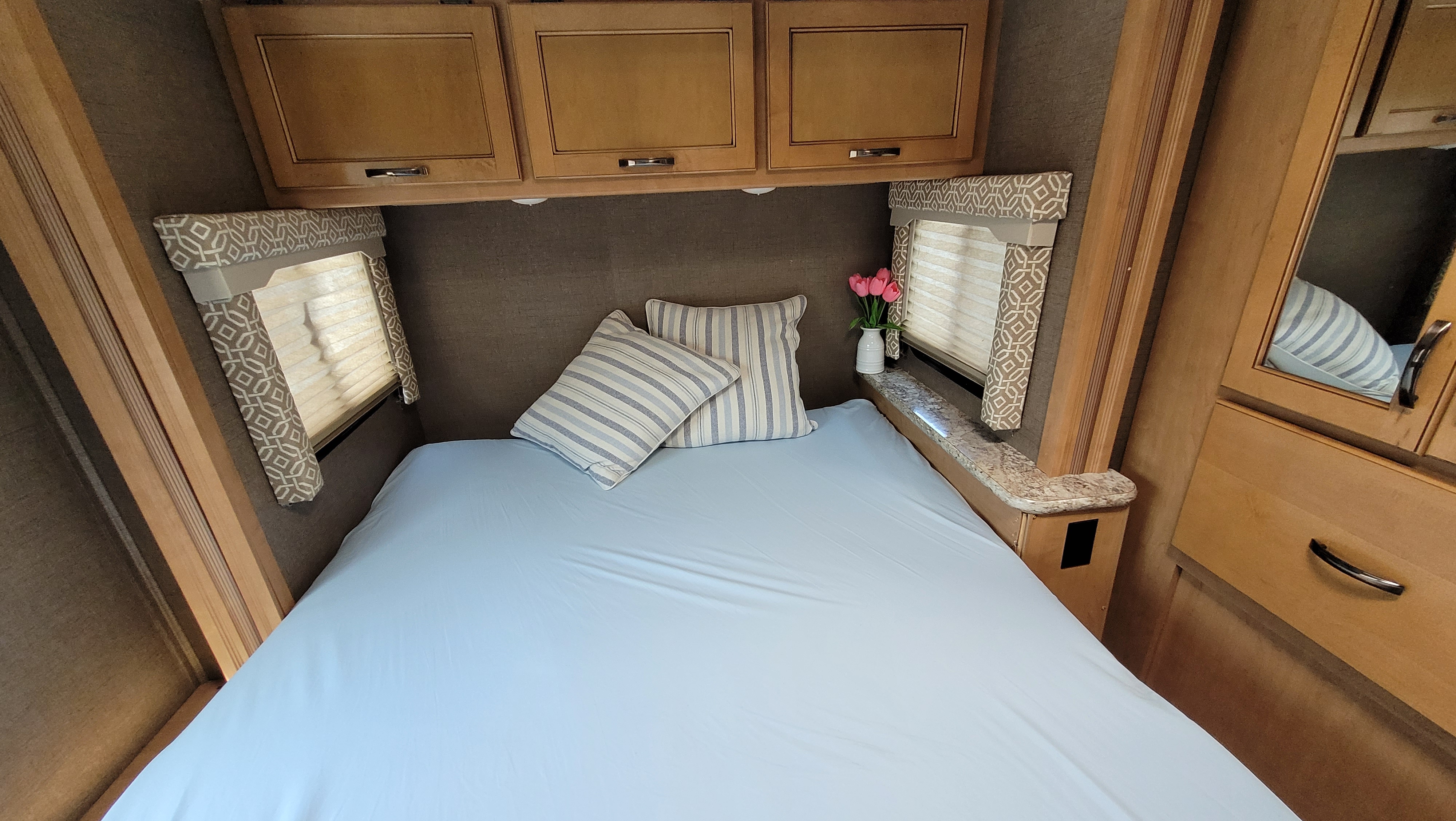 Cozy RV rental bedroom with light blue sheets, striped pillows, overhead cabinets, and window blinds.. Thor Freedom Elite 2017