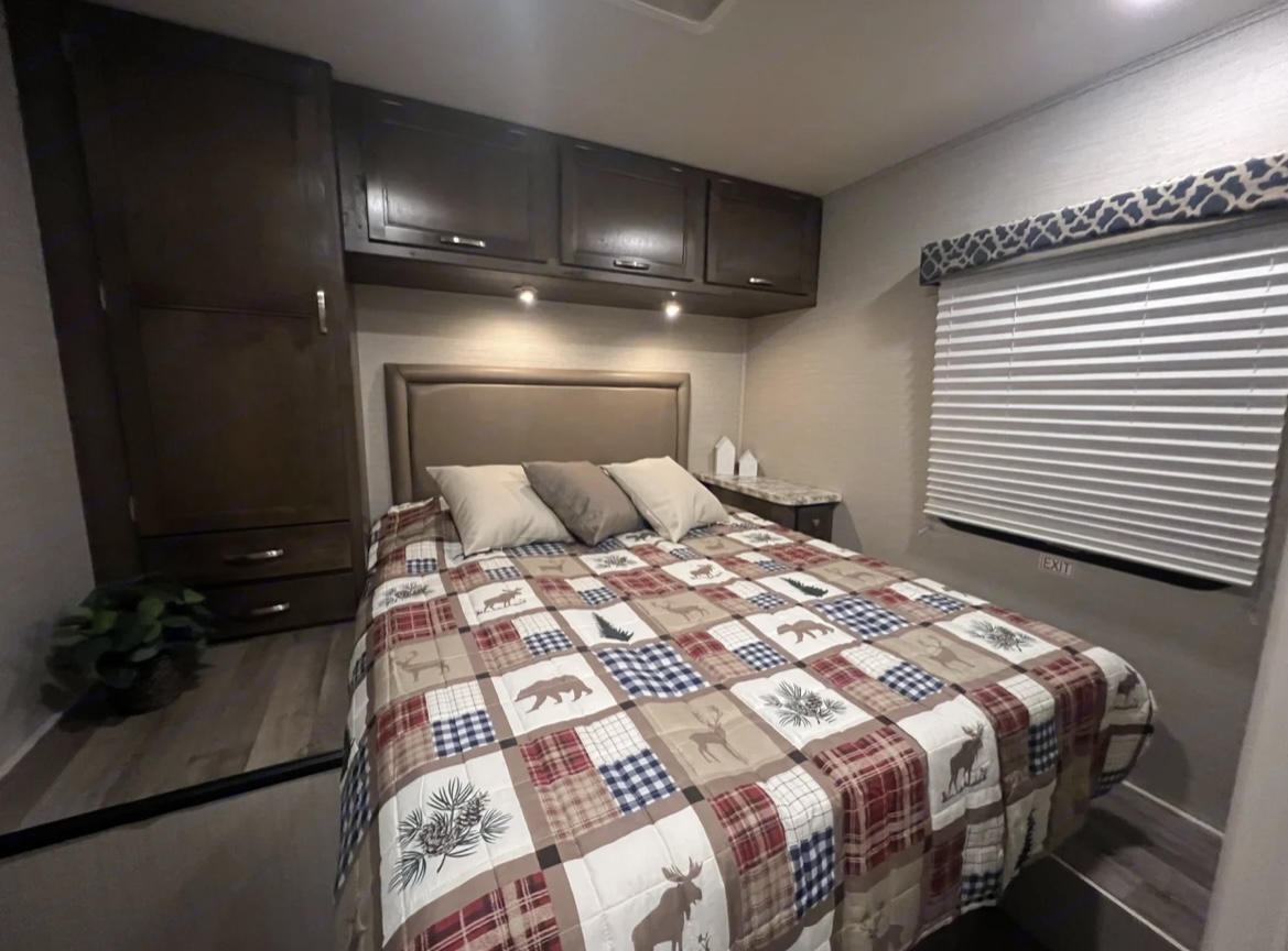 Cozy RV rental bedroom with rustic quilt, ample storage, and window blinds. Perfect for adventures.. Jayco Redhawk 2019