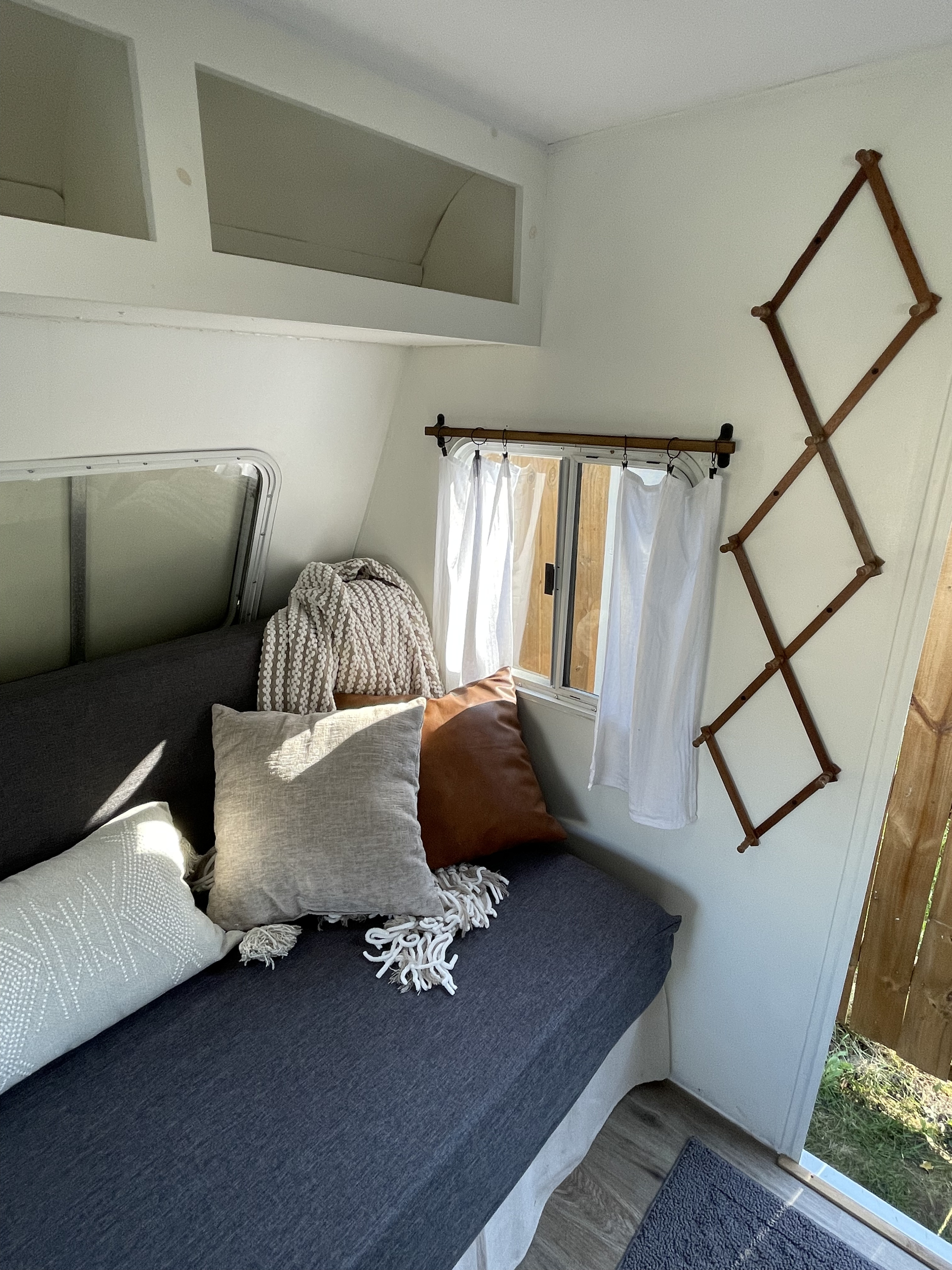 Bright RV rental interior: cozy sofa with neutral pillows, window with sheer curtains, shelves, and a decorative wooden rack.. R-Vision 7000 Series 1999