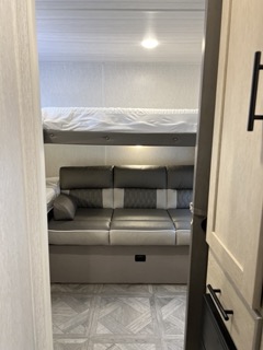 This RV rental interior features a cozy living space with a gray sofa and an overhead bunk bed, perfect for family travel.. Forest River Wildwood X-lite 273QBXL 2023