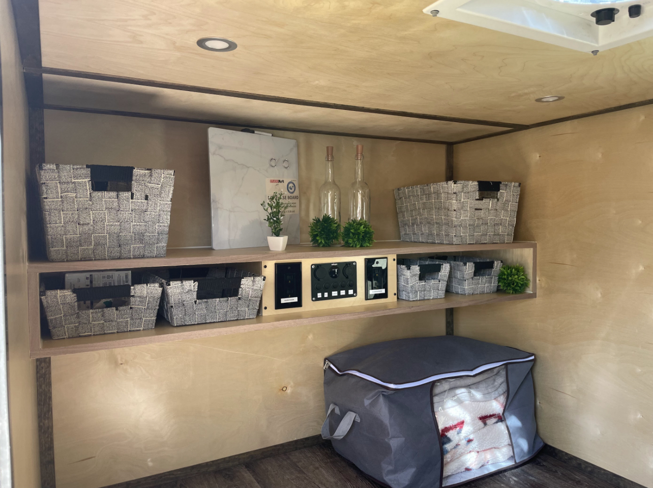 RV rental interior featuring smart storage solutions: woven baskets, a control panel, and a soft bag for bedding.. Pura Vida Overland PV1 2022