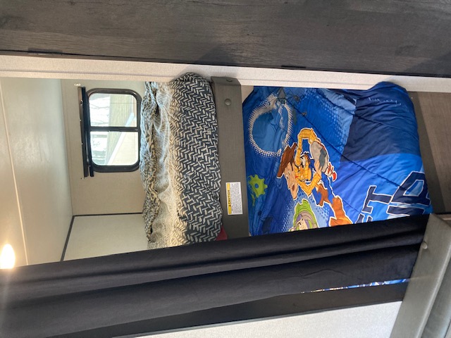 Cozy RV rental bunk beds for sleeping. Lower bunk has blue Toy Story bedding; upper has a gray patterned blanket. Window visible.. Keystone RV Hideout 2021