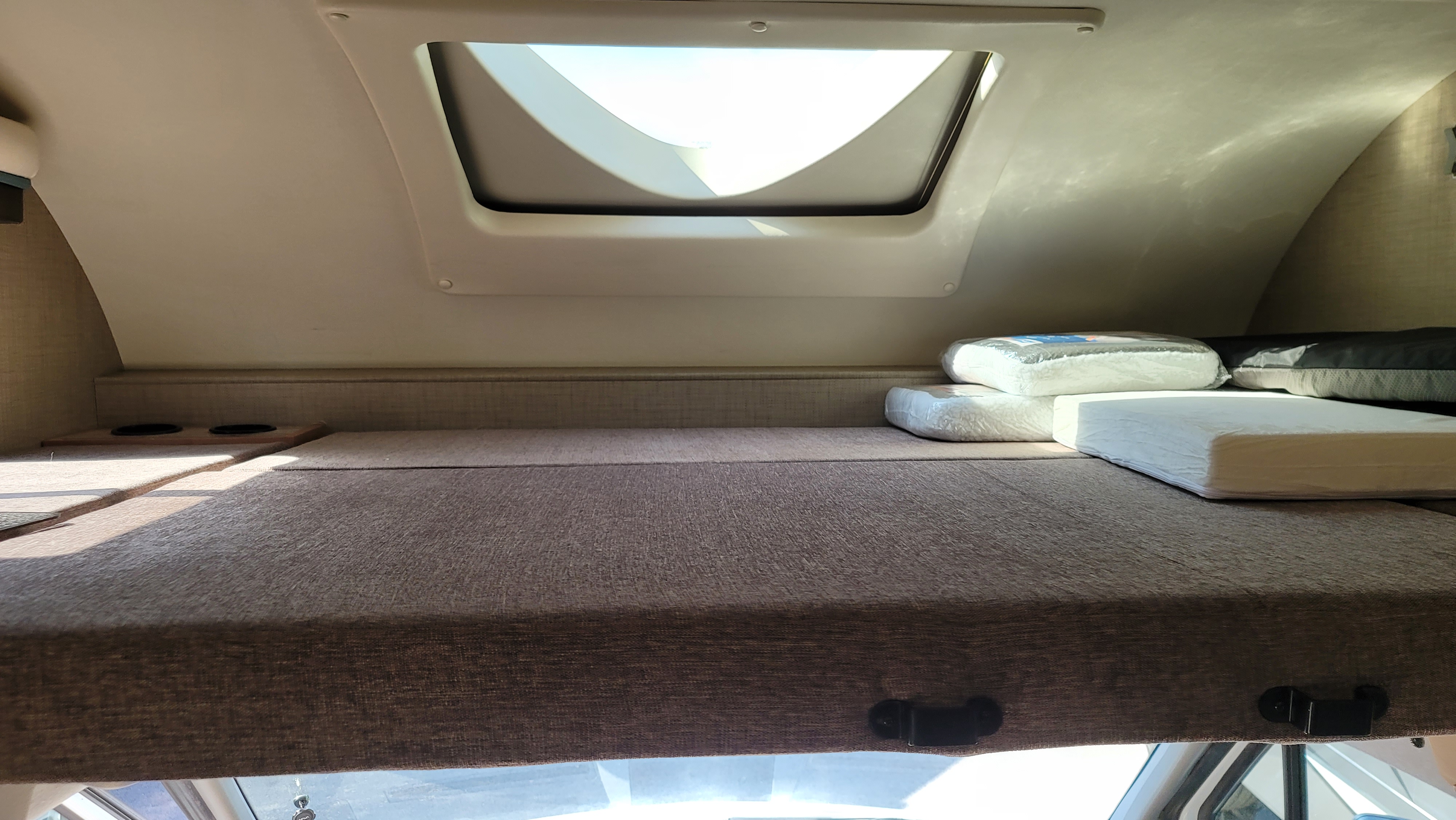RV rental's cab-over bunk: a spacious sleeping area with brown fabric, cupholders, skylight, and stacked bedding.. Thor Quantum 2019