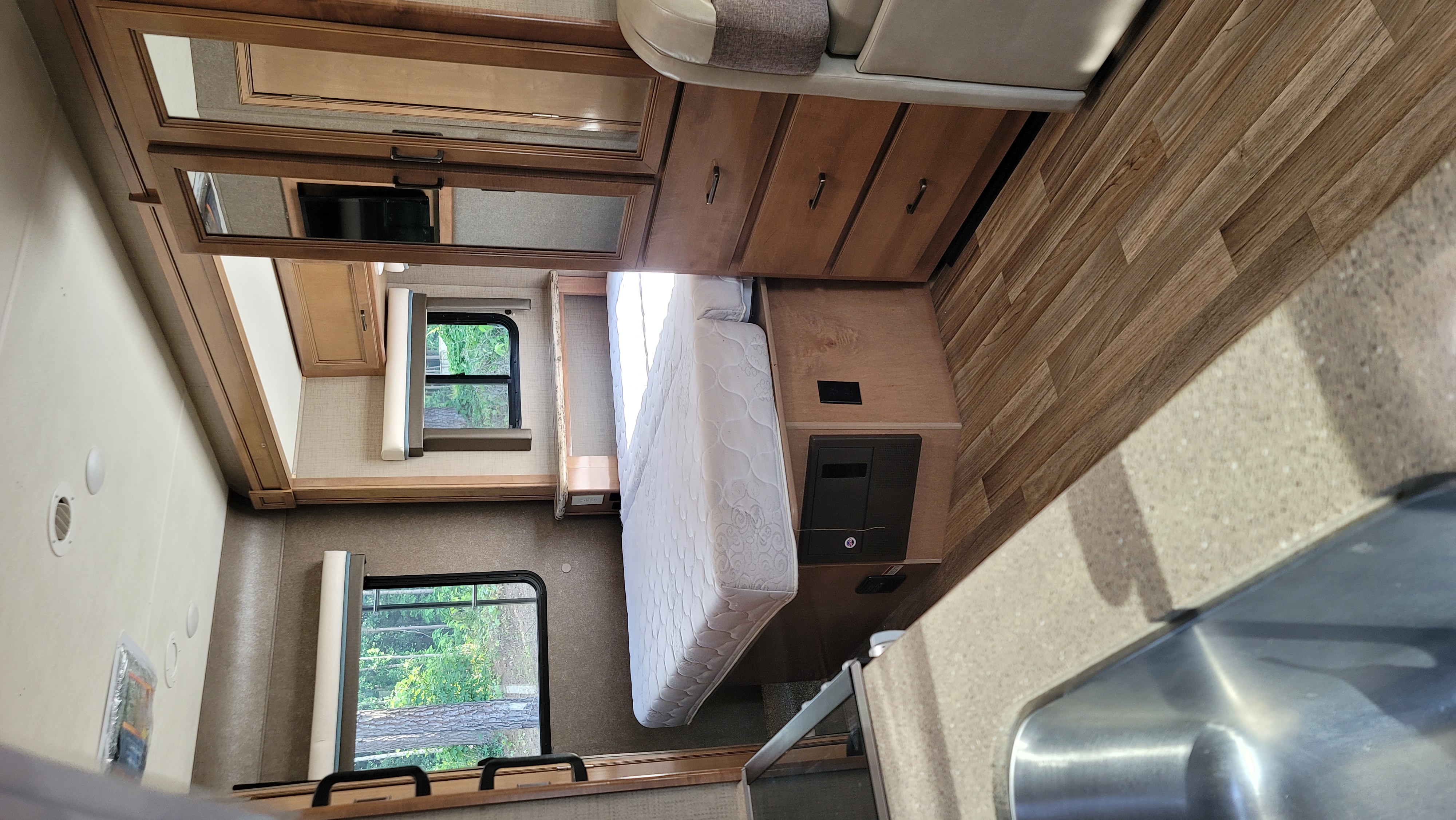 RV rental interior: A cozy bedroom with mattress and windows, overhead mirrored cabinets, and a compact kitchen sink area.. Thor Quantum 2019