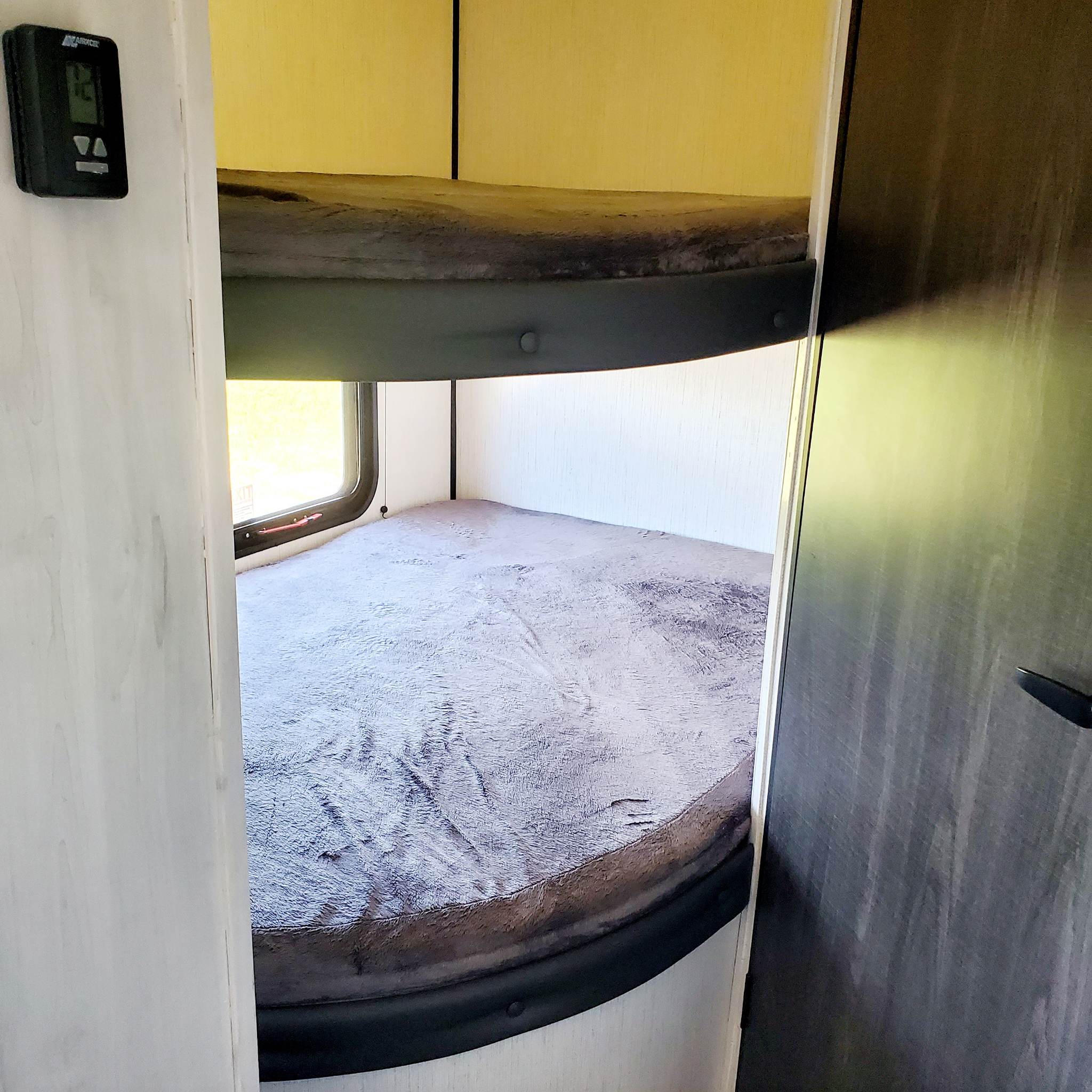 RV rental bunk beds with soft bedding. A thermostat is on the left wall, and a window is by the lower bunk.. Heartland 261 JM 2023