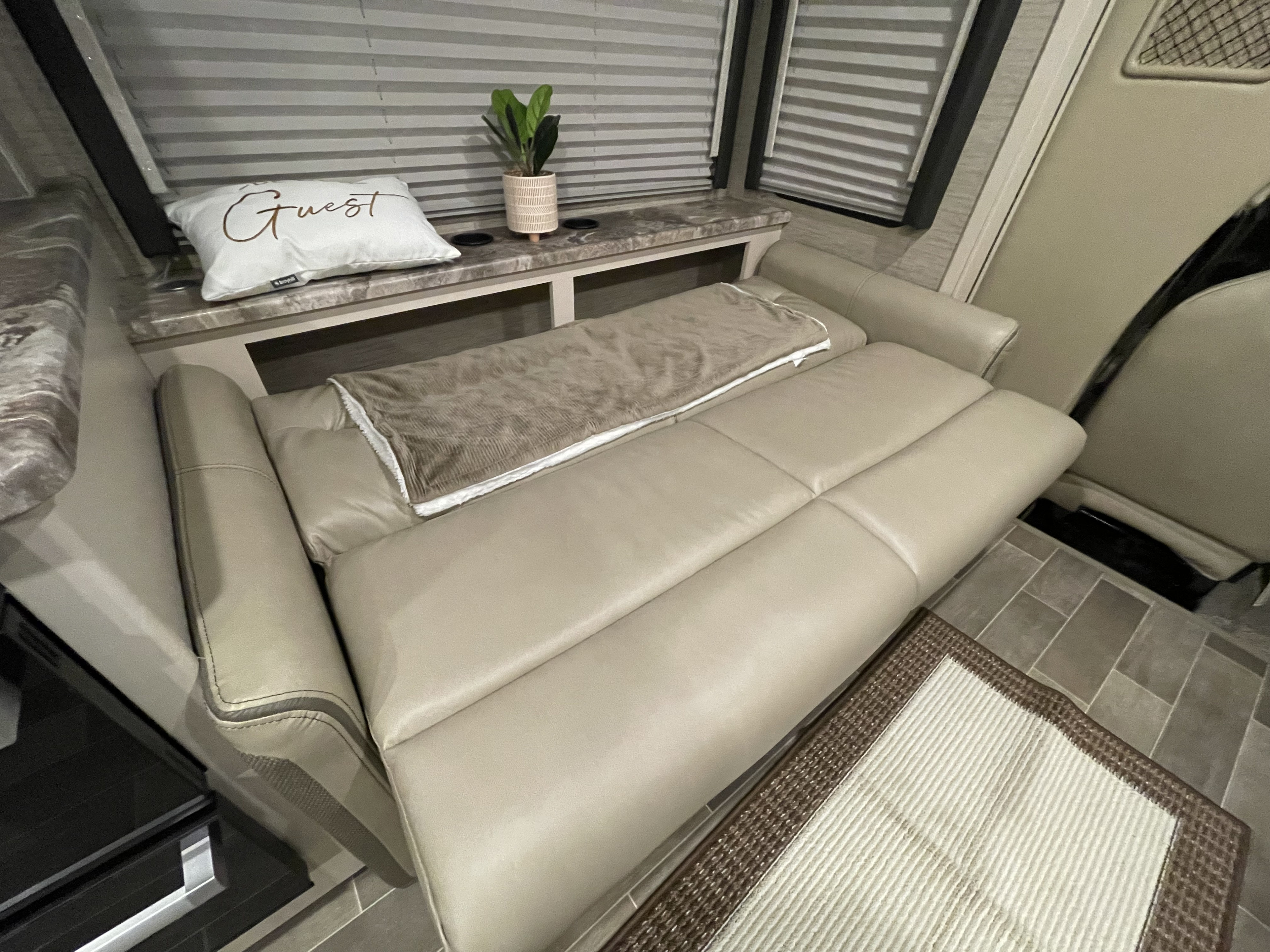 Inside an RV rental: a light-colored sofa (likely convertible to bed) with blanket, counter holding 'Guest' pillow & plant.. Thor Chateau 2022